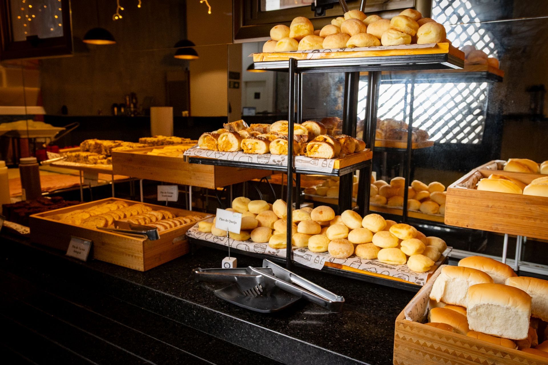 Balcão expositor de pães com diversos tipos de pão em prateleiras de vários níveis.