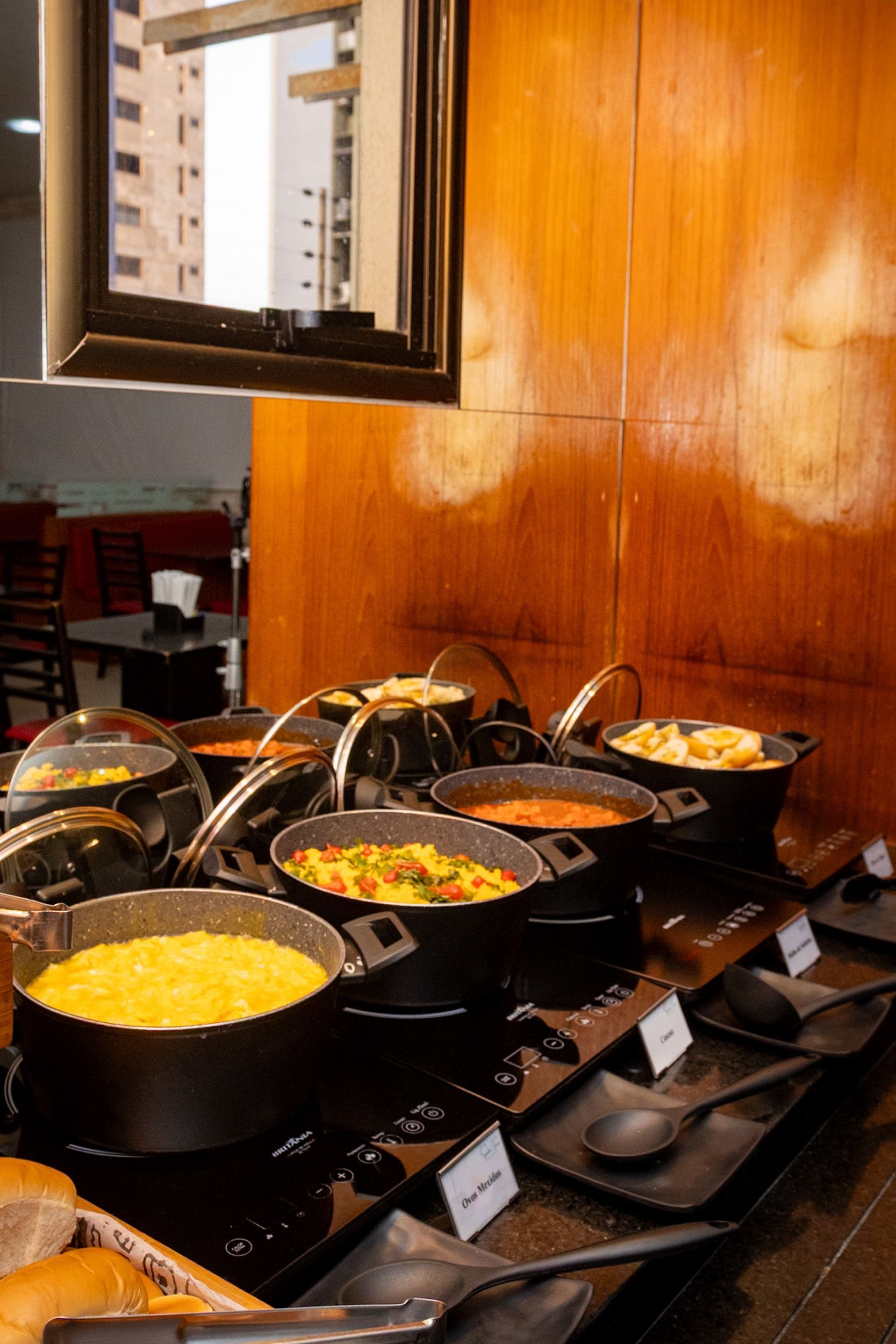 Buffet com diversos pratos servidos em travessas pretas sobre uma superfície de madeira, ambiente de restaurante.