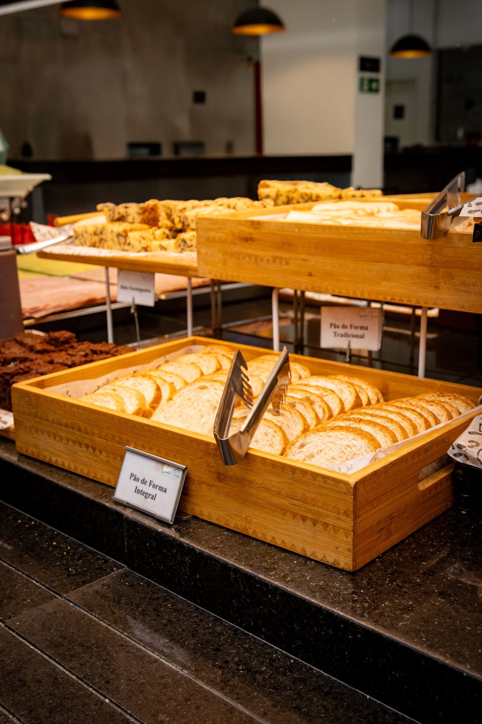 Pães e doces em bandejas de madeira sobre uma mesa de bufê, prontos para servir.