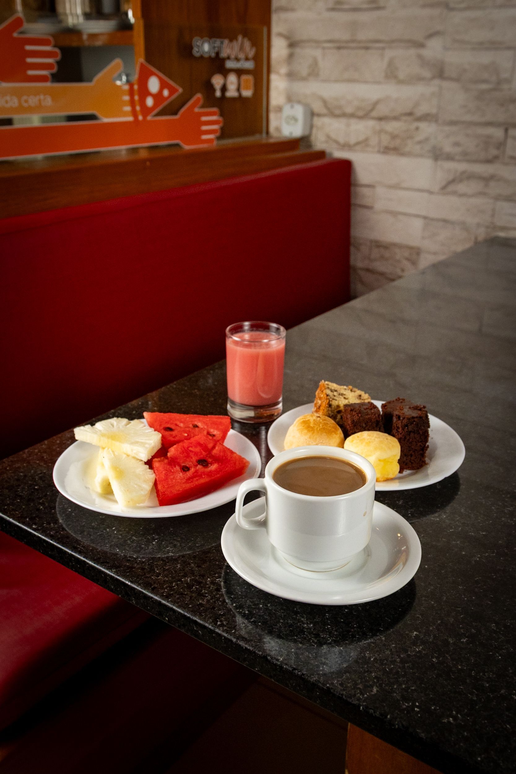 Café da manhã servido em uma mesa: prato de frutas, doces, café e um smoothie.