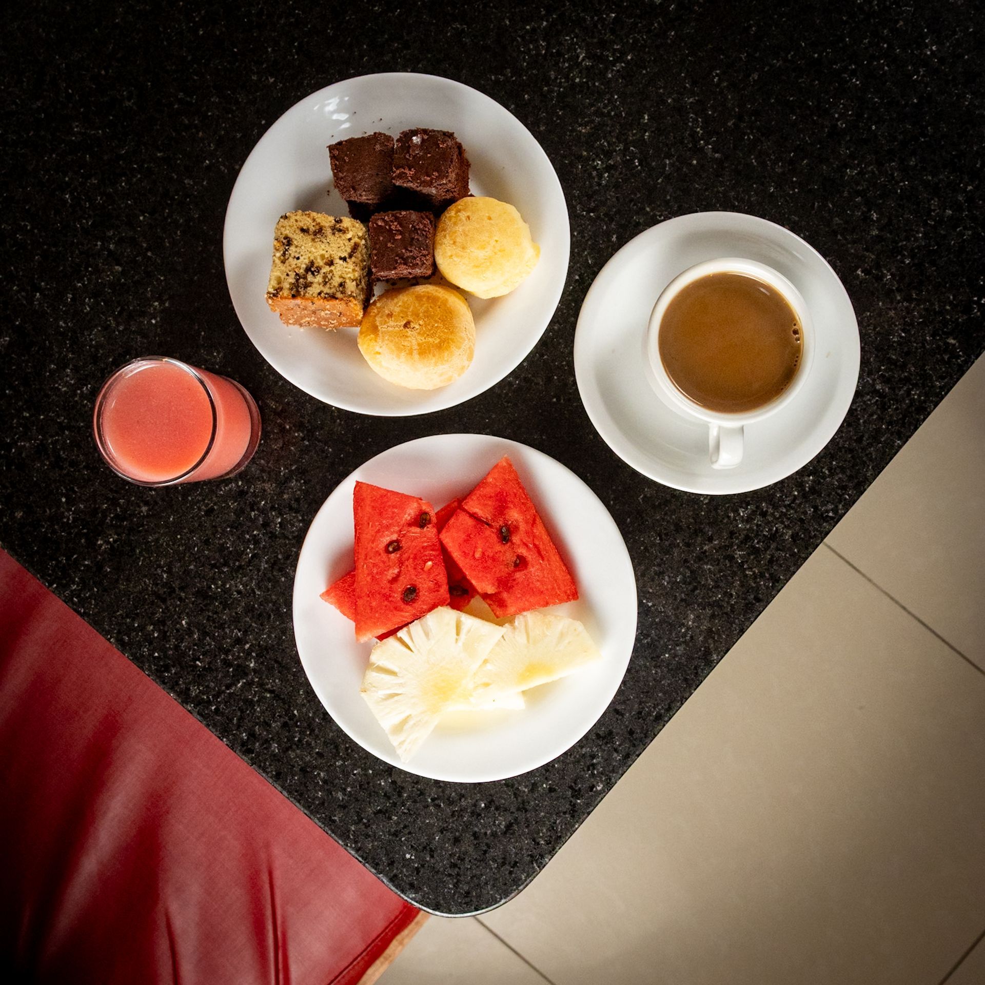 Café da manhã com frutas, doces, café e suco em uma mesa preta com pintas.