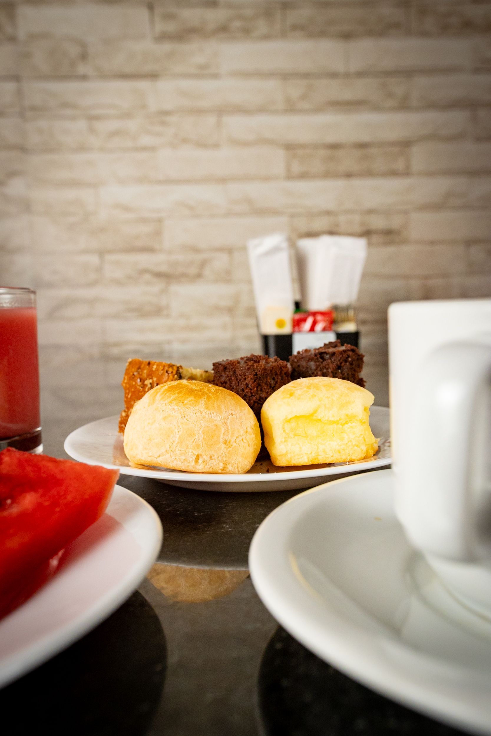 Mesa de café da manhã com um prato de doces, uma xícara de café e um copo de suco.