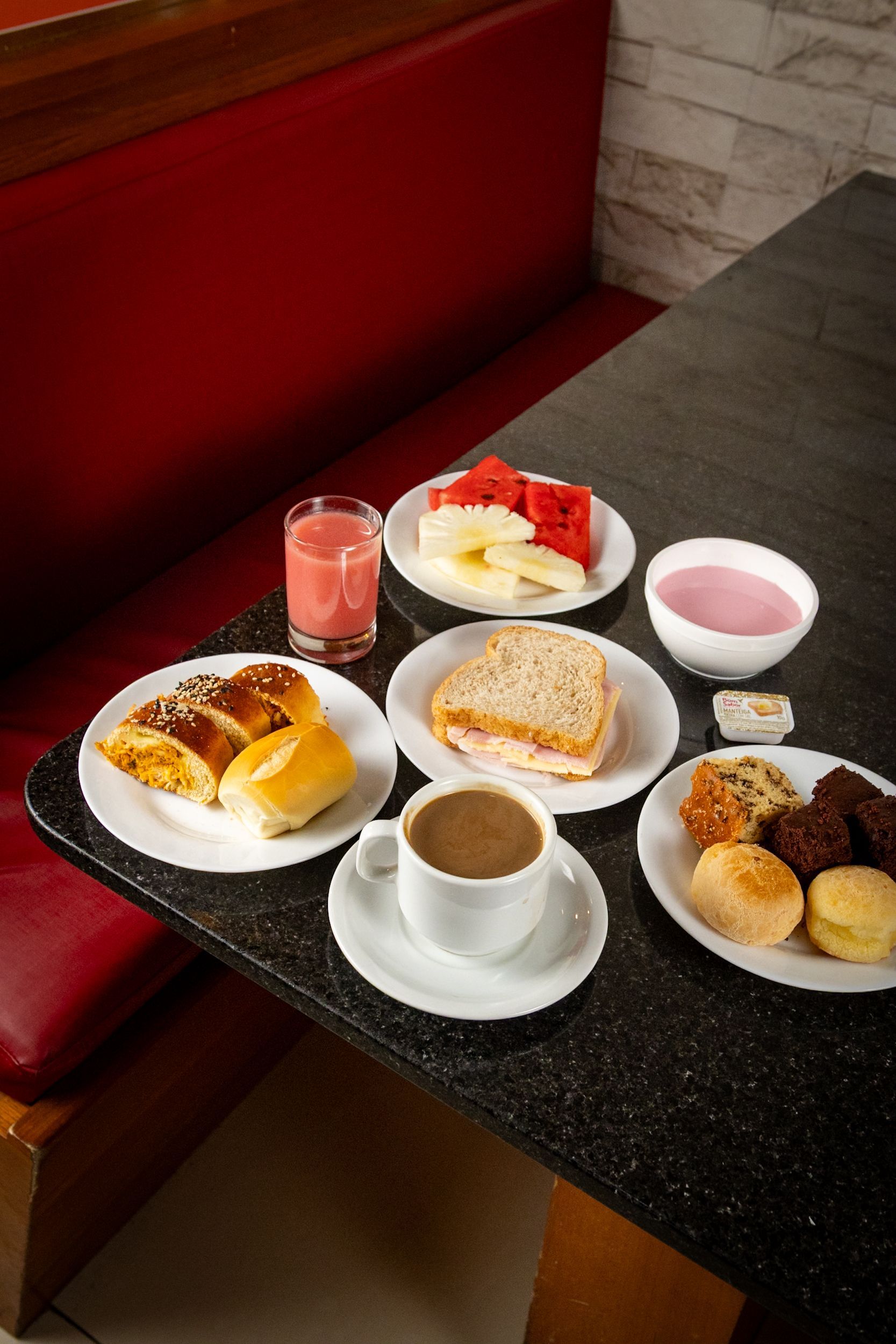 Café da manhã servido na mesa: café, suco, doces, frutas, iogurte e um sanduíche.