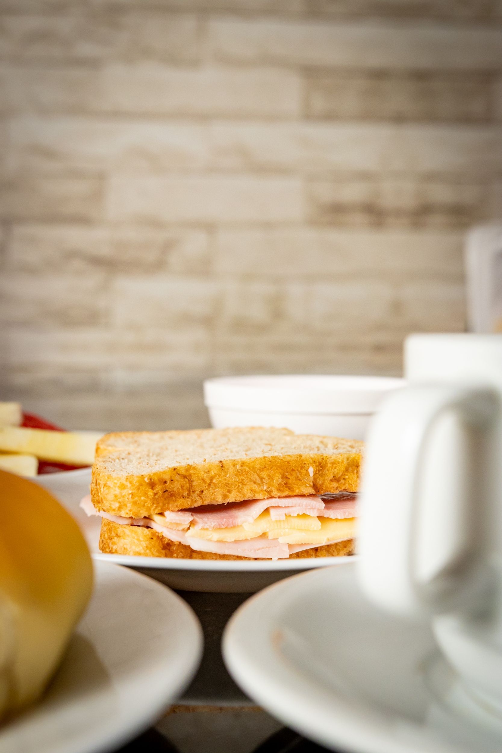 Sanduíche de presunto e queijo em um prato com outros itens de café da manhã, tendo como fundo de madeira.