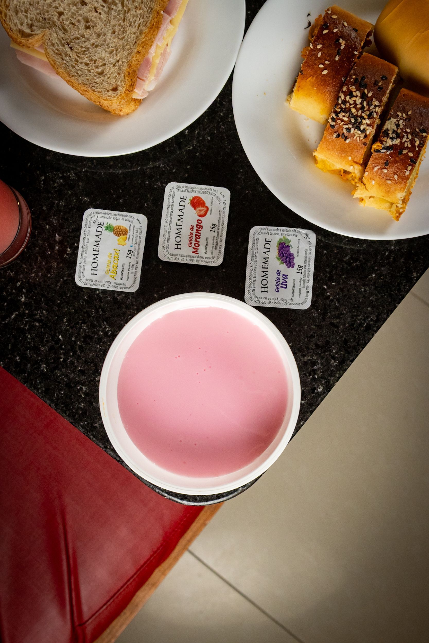 Bebida rosa em uma tigela branca, petiscos e pequenos quadrados de vidro decorativos sobre uma superfície escura.