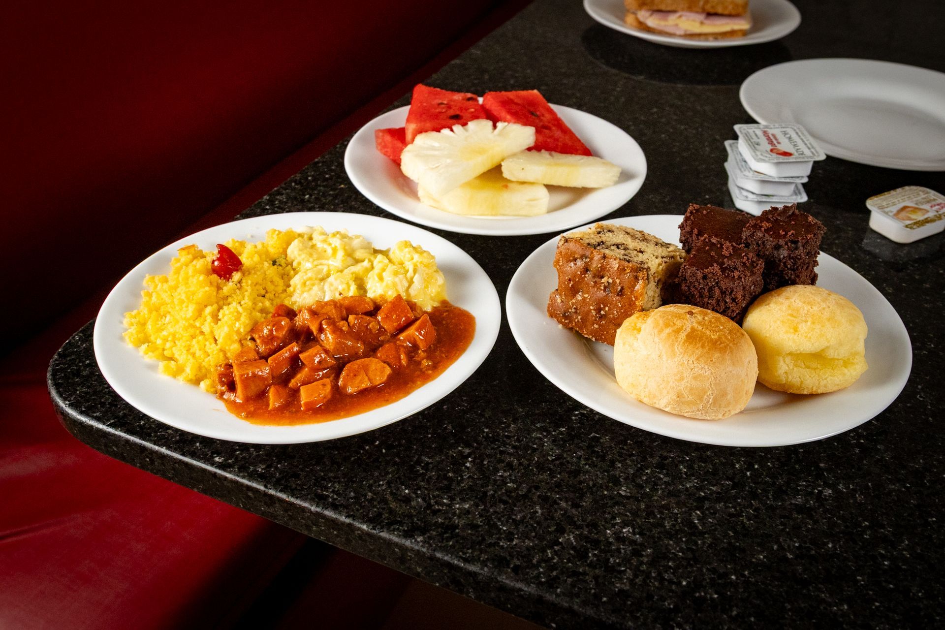 Pratos de comida sobre uma mesa: ovos, guisado, fatias de frutas, doces e pão.