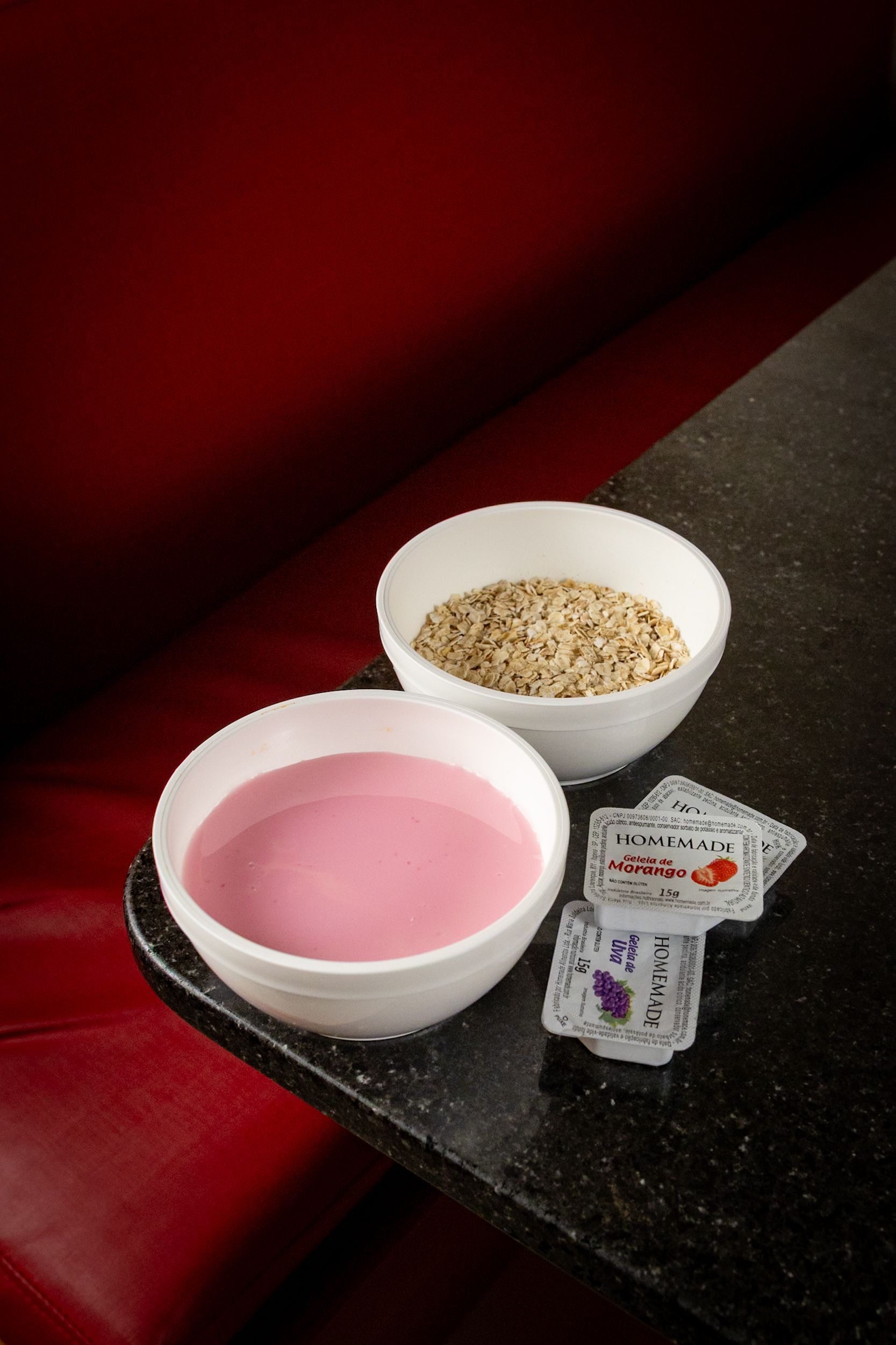Duas tigelas brancas: uma com líquido rosa, a outra com um líquido marrom granulado; cartas sobre uma mesa preta, fundo vermelho para a cabine.