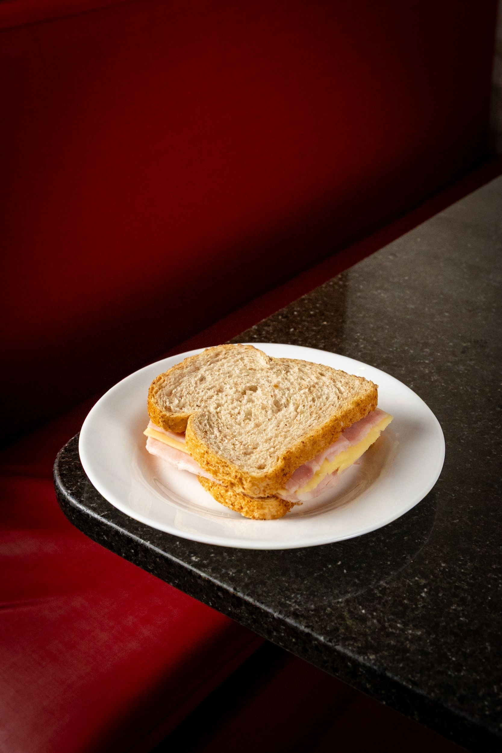 Sanduíche de presunto em um prato branco, sobre uma mesa preta com uma cabine vermelha ao fundo.