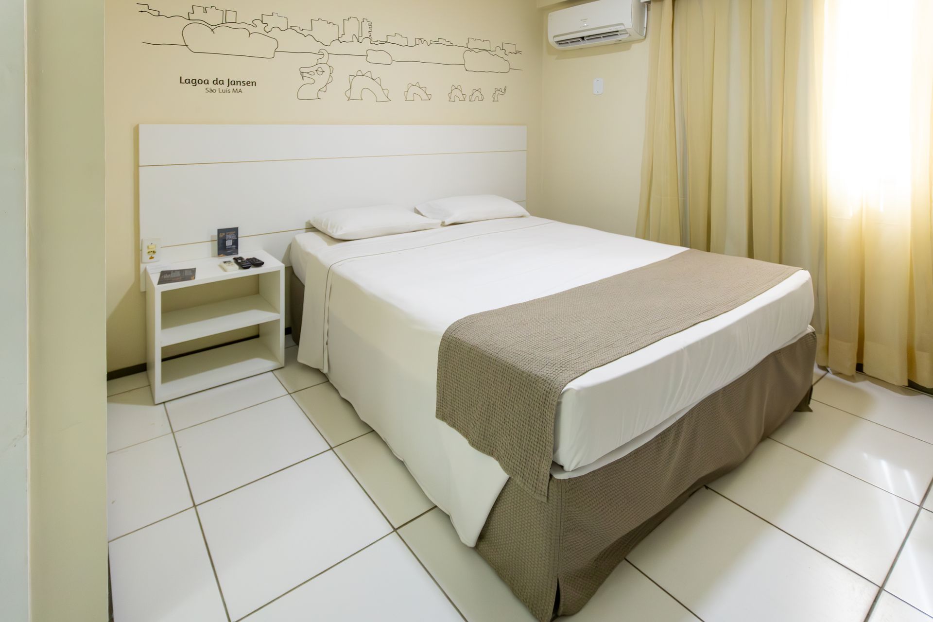 Quarto com paredes brancas, uma cama de casal e uma pequena mesa de cabeceira.