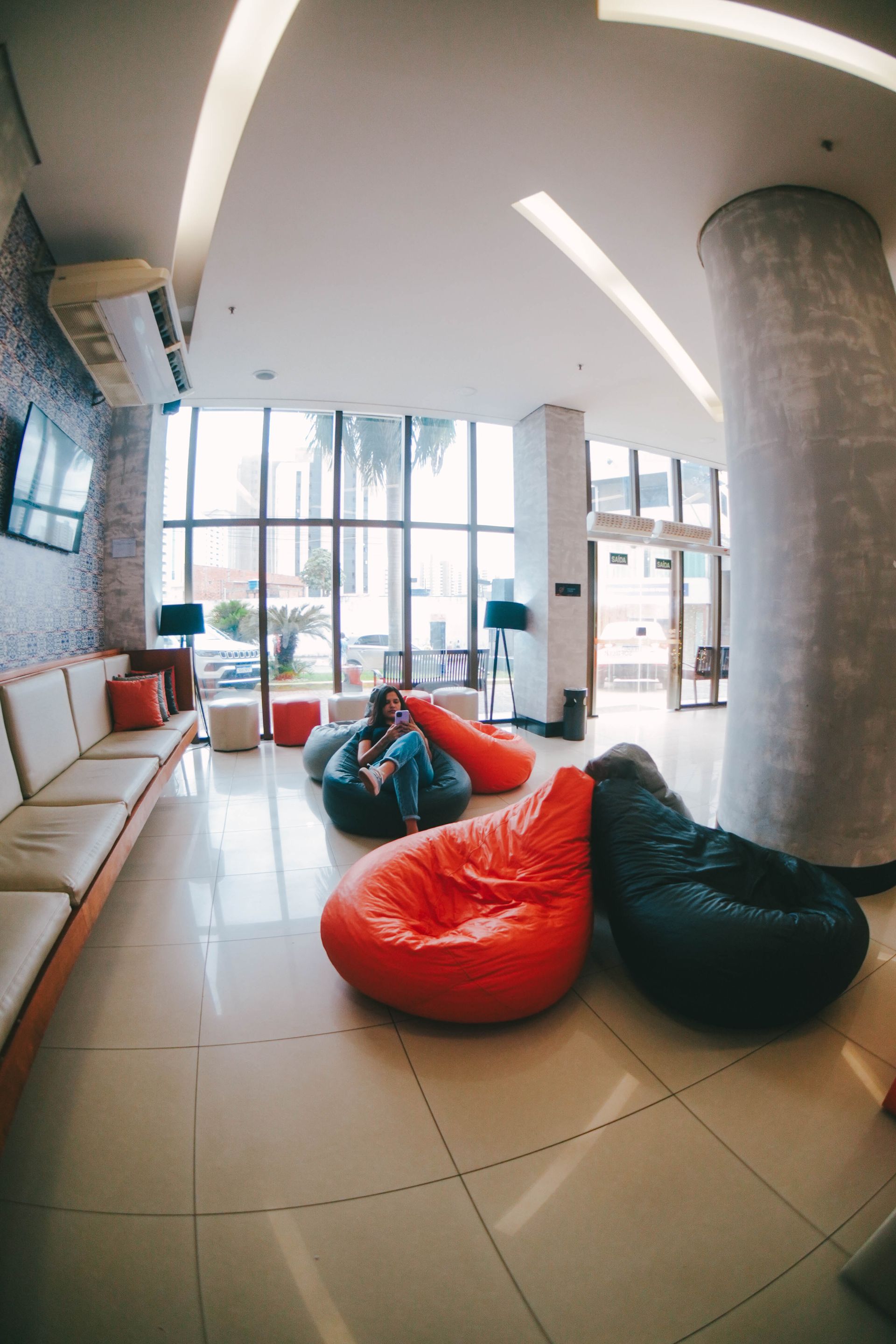 Hall de entrada com pufes e assentos. Janelas amplas e um sofá comprido. Paleta de cores neutras.