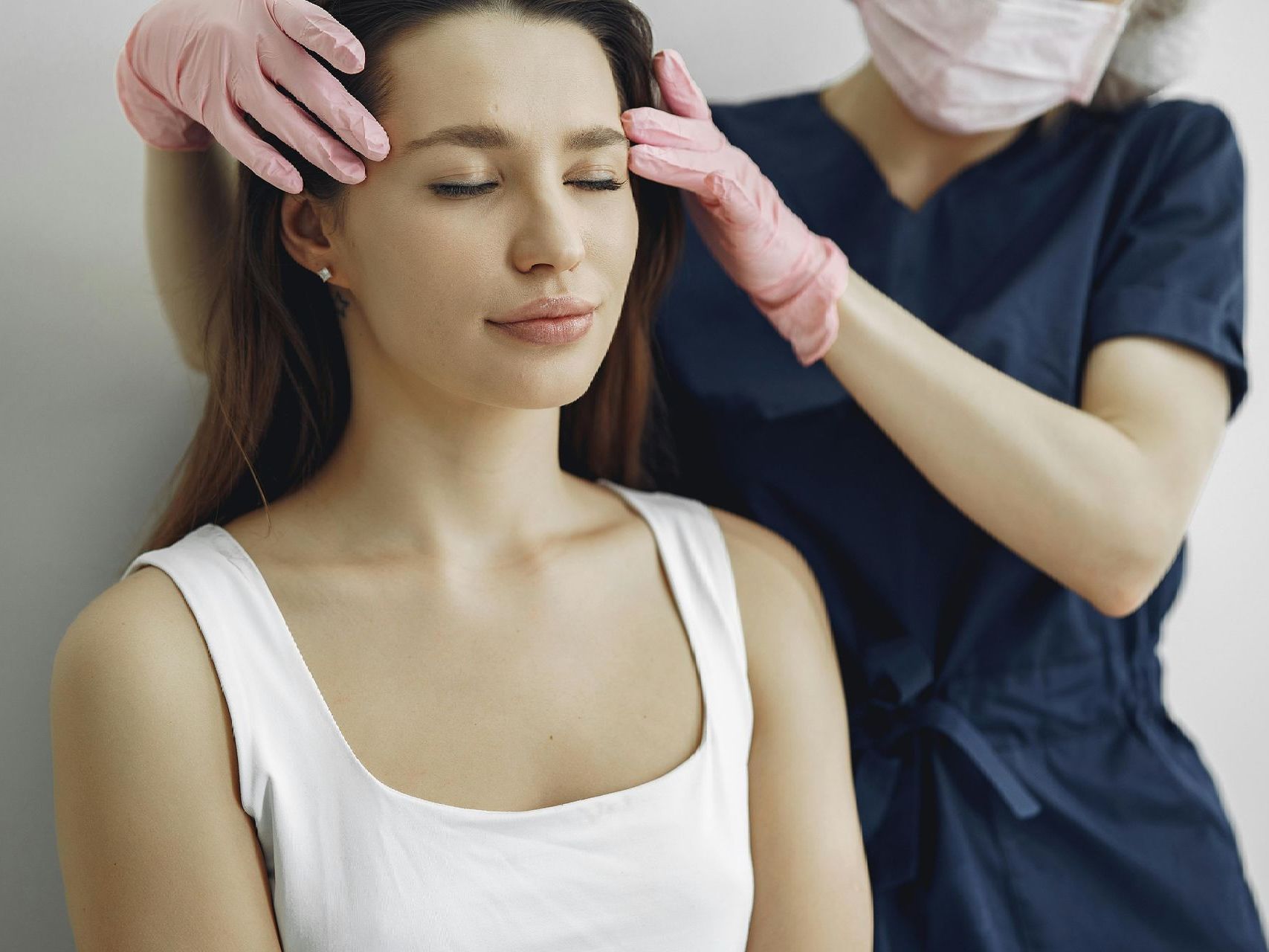 A woman is getting a head massage from a doctor wearing a mask and gloves.