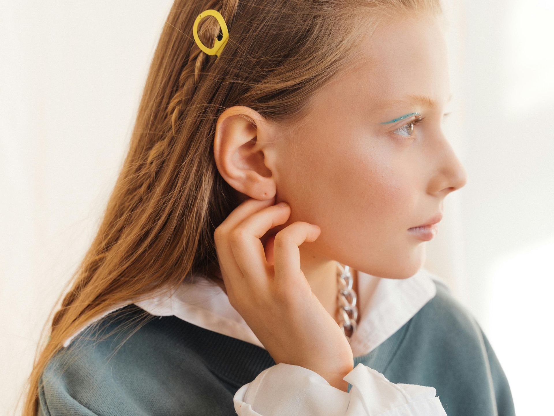 A young girl with a braid in her hair is touching her ear.