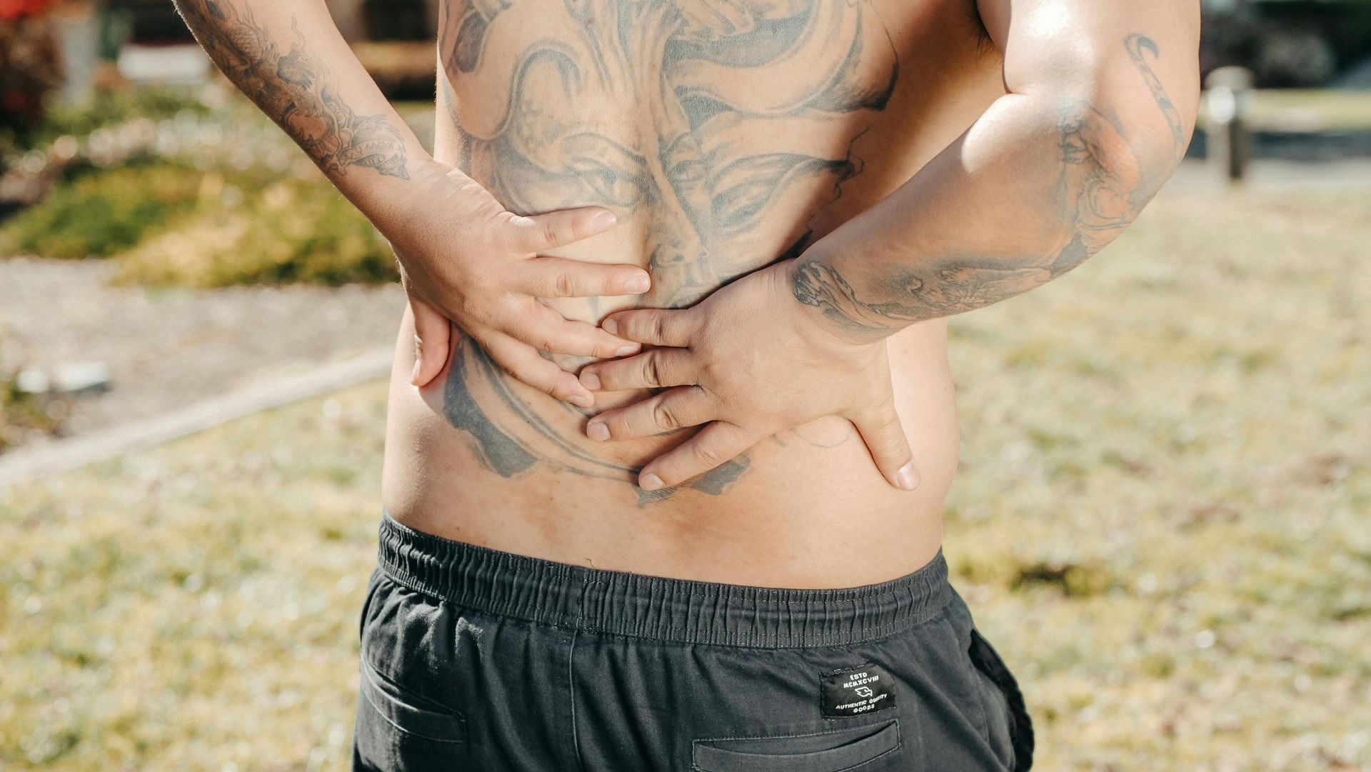 A man with a tattoo on his back is holding his back in pain.