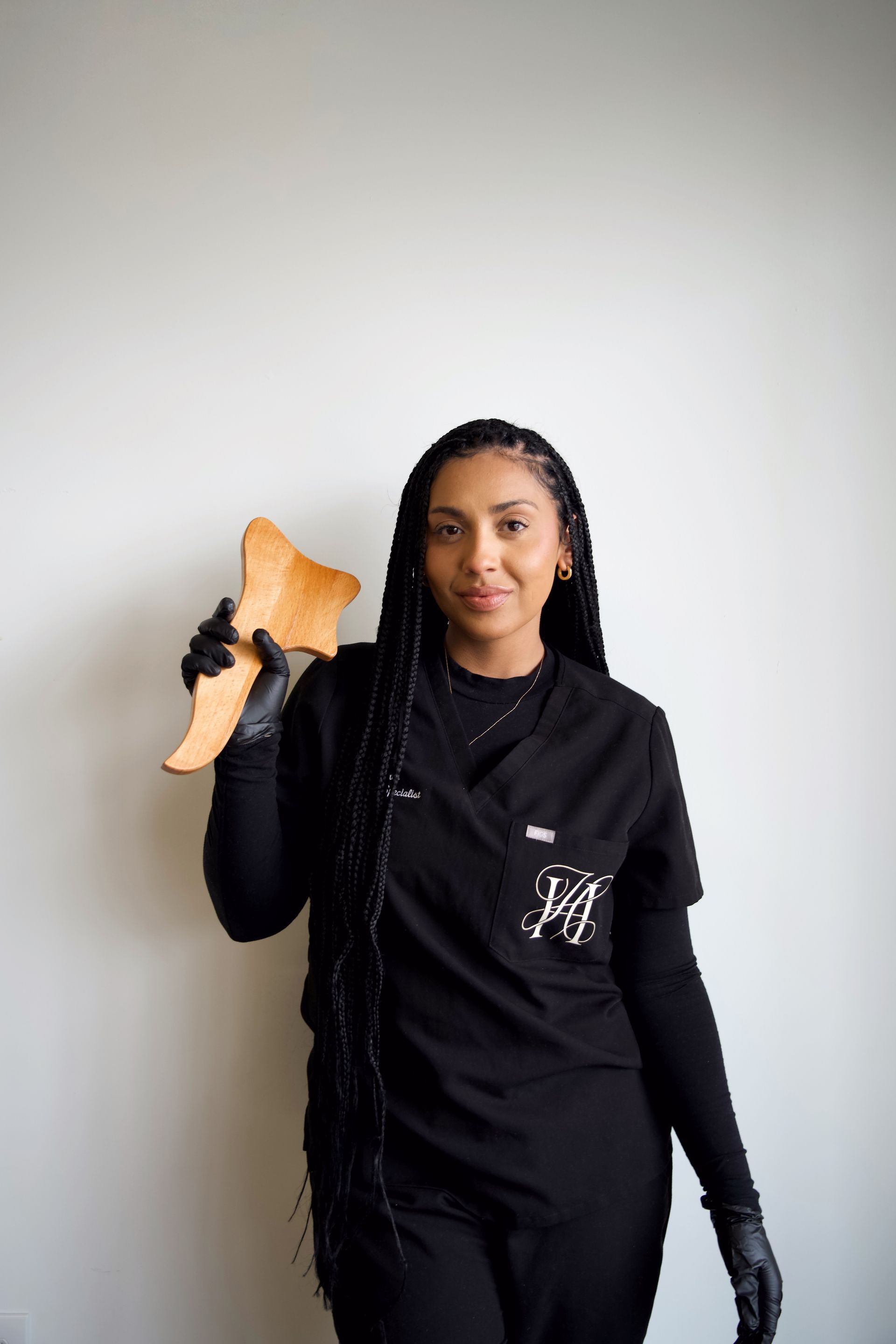 A woman in a black scrub top is holding a piece of wood.