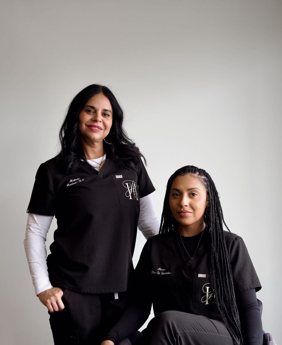 Two women in scrubs are posing for a picture while one is sitting in a chair.