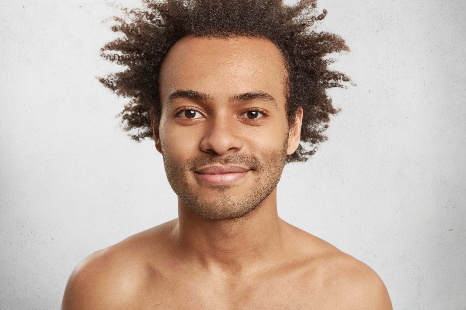 A shirtless man with curly hair is smiling for the camera.