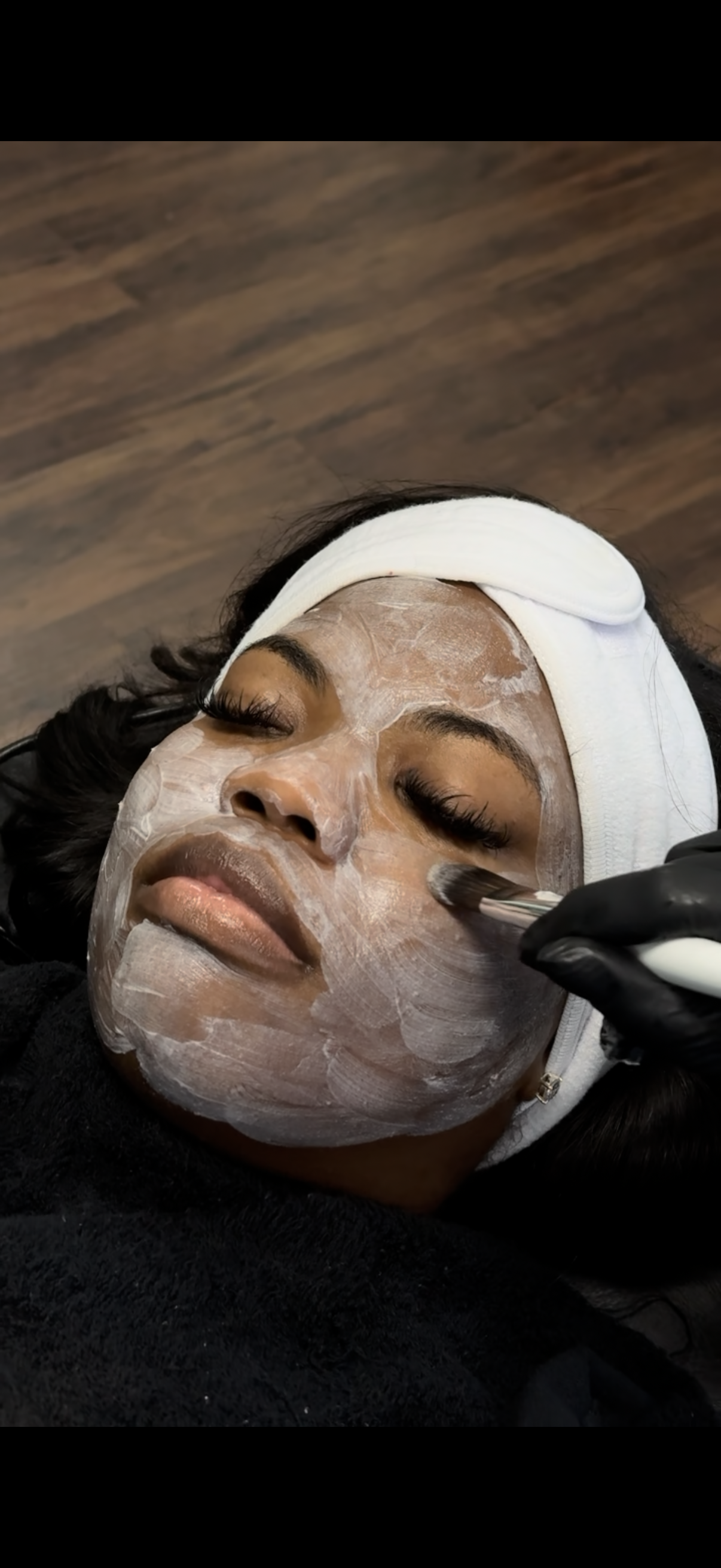 A person receiving a facial treatment. A mask covers their face. A gloved hand holds a tool near their eye.