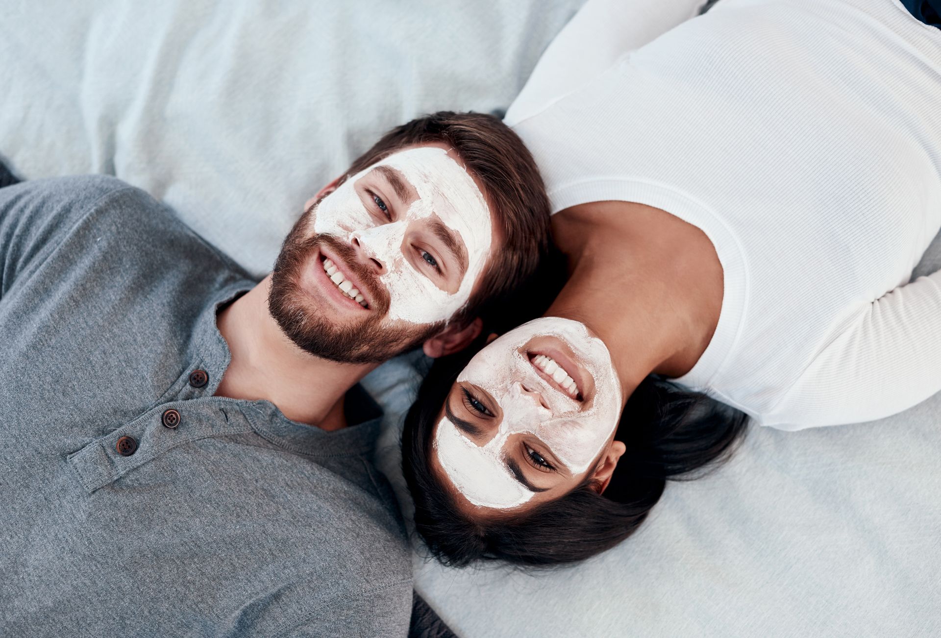 A man and a woman are laying on a bed with face masks on their faces.