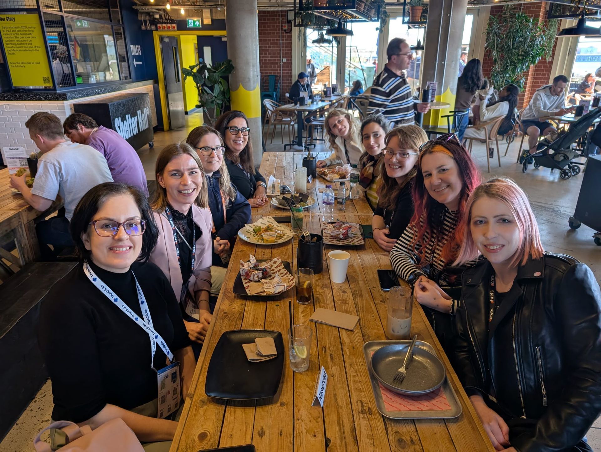 A group of WTS ladies are sitting at a long wooden table in a restaurant.