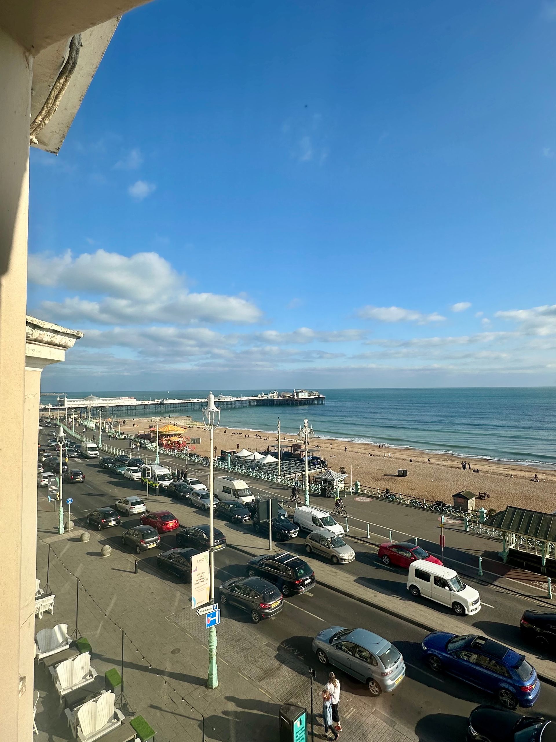 A view of a beach from a balcony with cars parked on the side of the road.