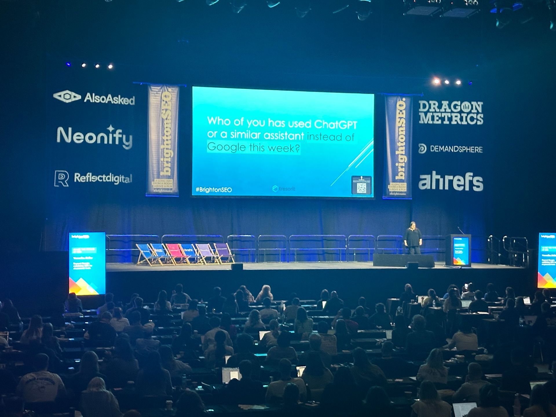A woman stands on a stage in front of a large screen that says neonify and ahrefs