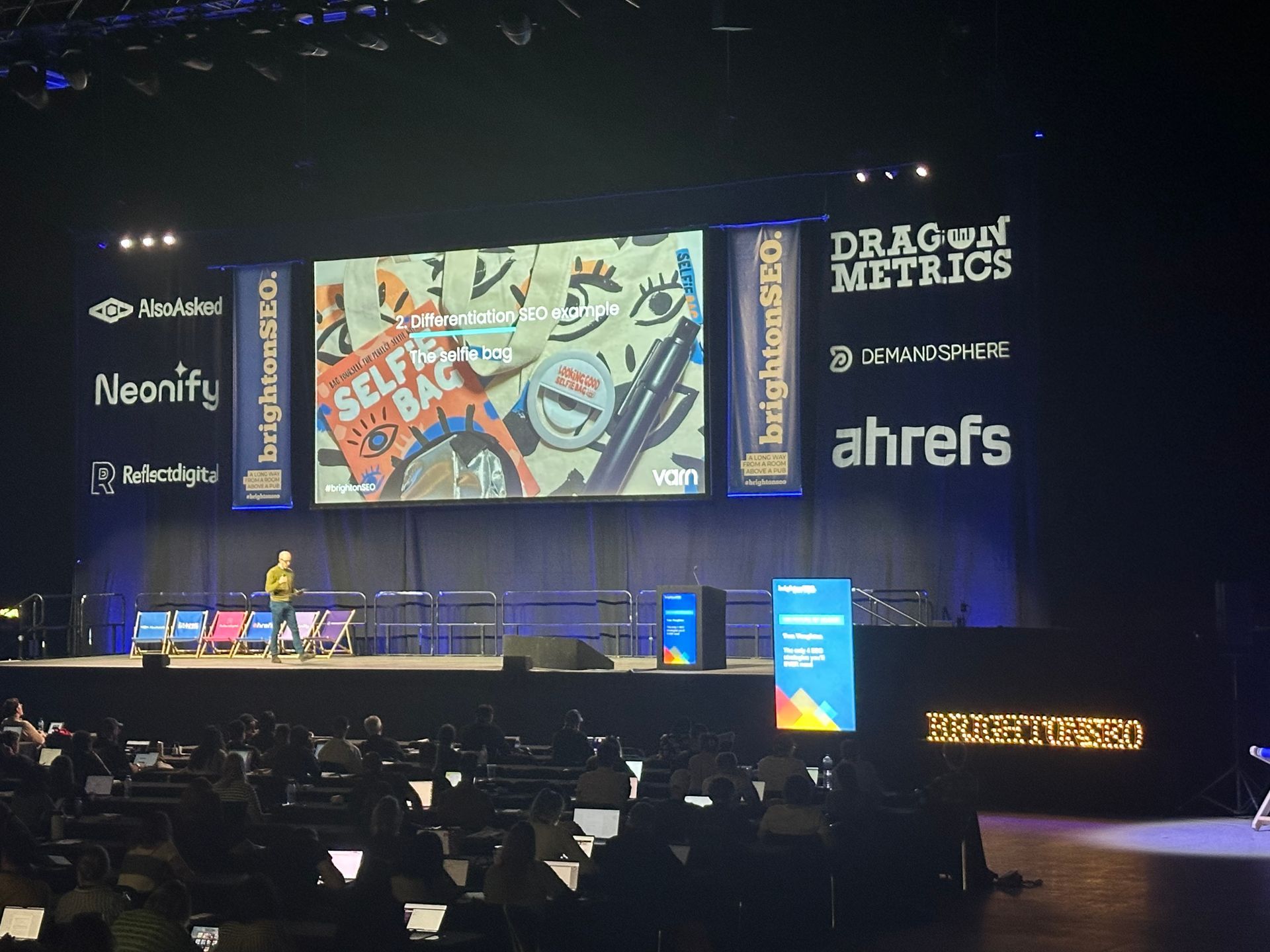 A man stands on a stage in front of a large screen that says dragon metrics