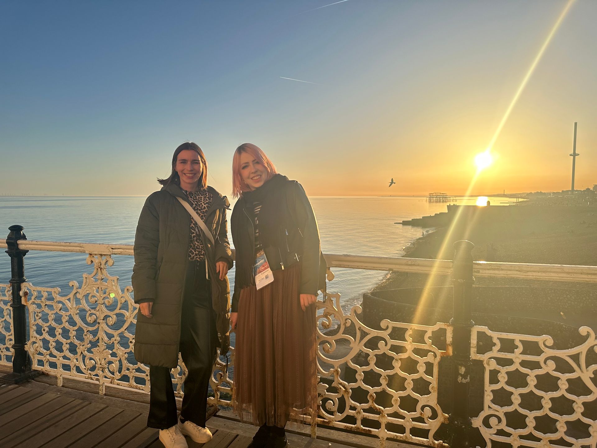 Two women are standing on a pier overlooking the ocean at sunset.