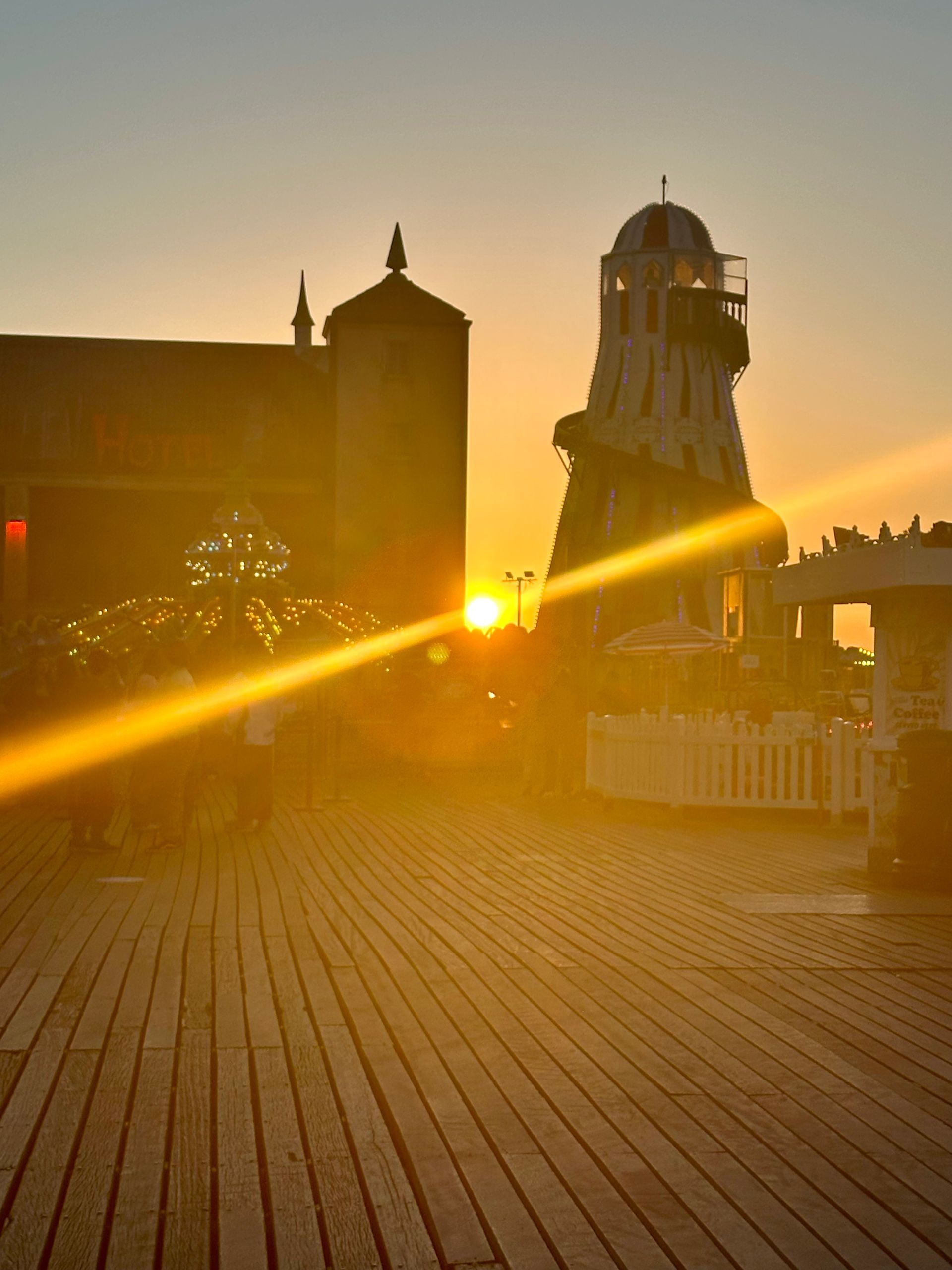 A sunset over a pier with a lighthouse in the background