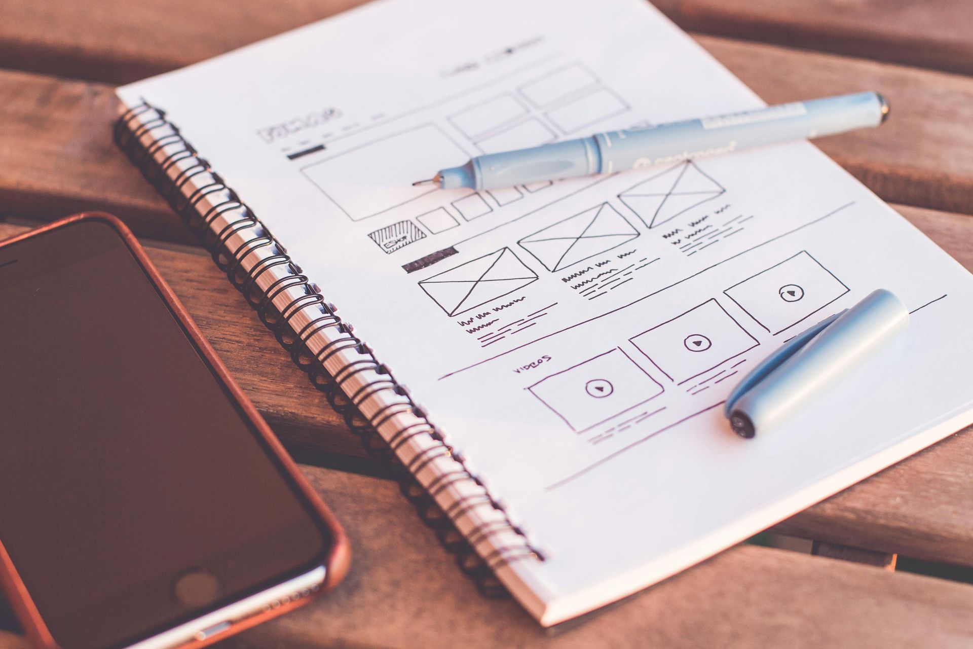 Notebook with wireframe sketches and pens beside a smartphone on a desk