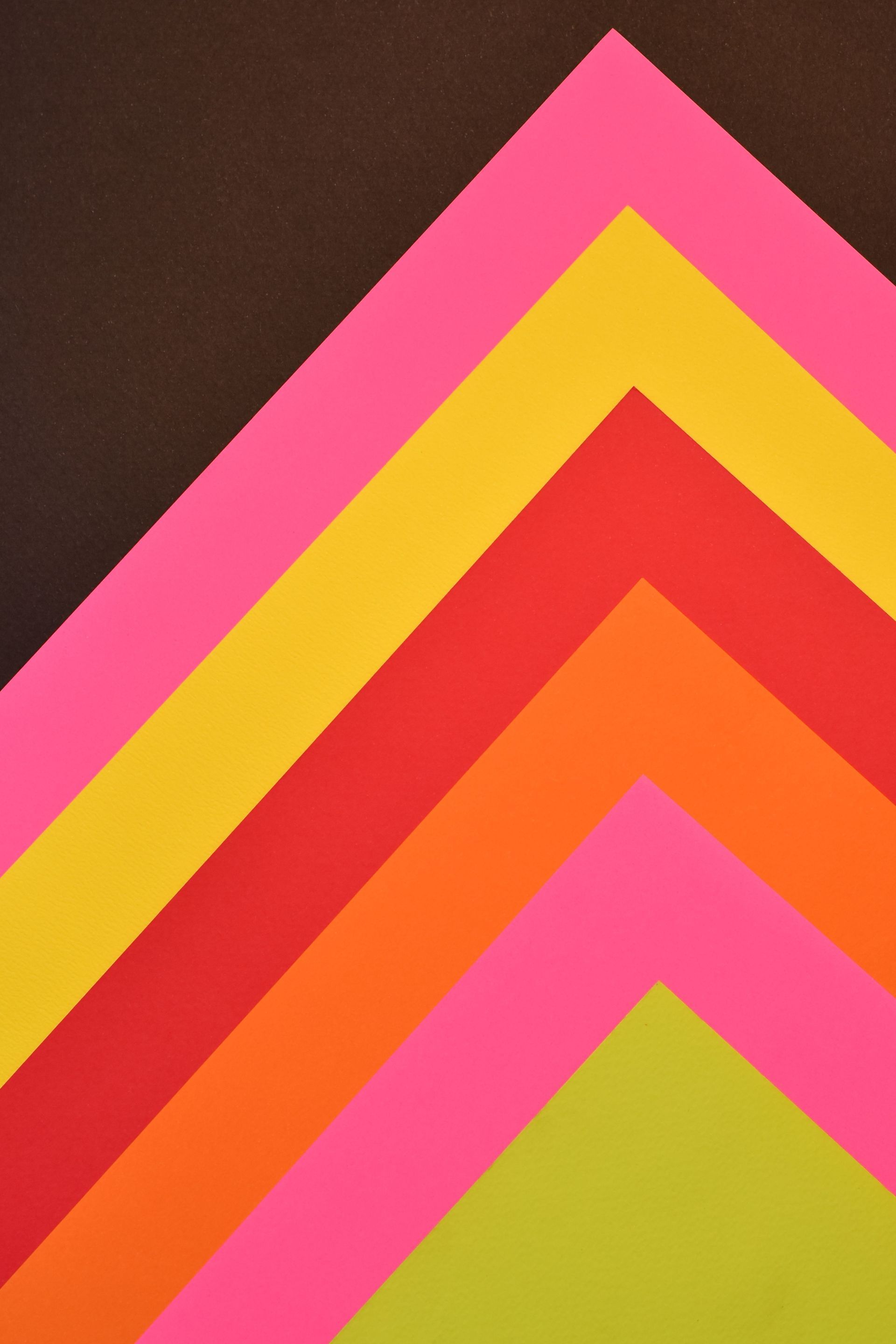 Colorful chevron pattern with layered pink, yellow, red, orange, and green stripes on a dark background