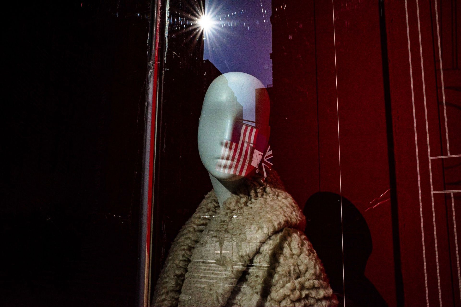 Mannequin in a fur coat against a glossy red wall with bright reflections and shadows
