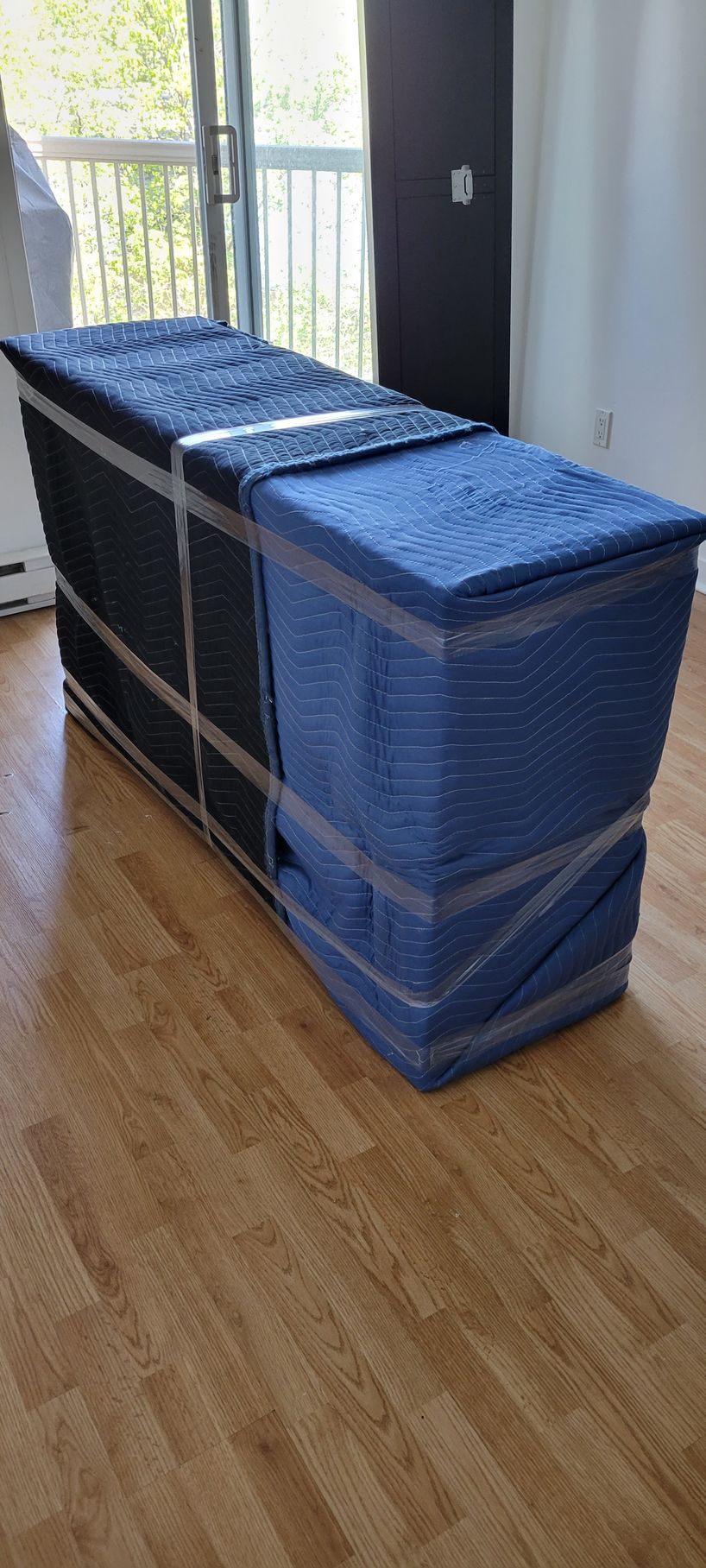 Une boîte bleue enveloppée de plastique est posée sur un plancher en bois dans un salon.