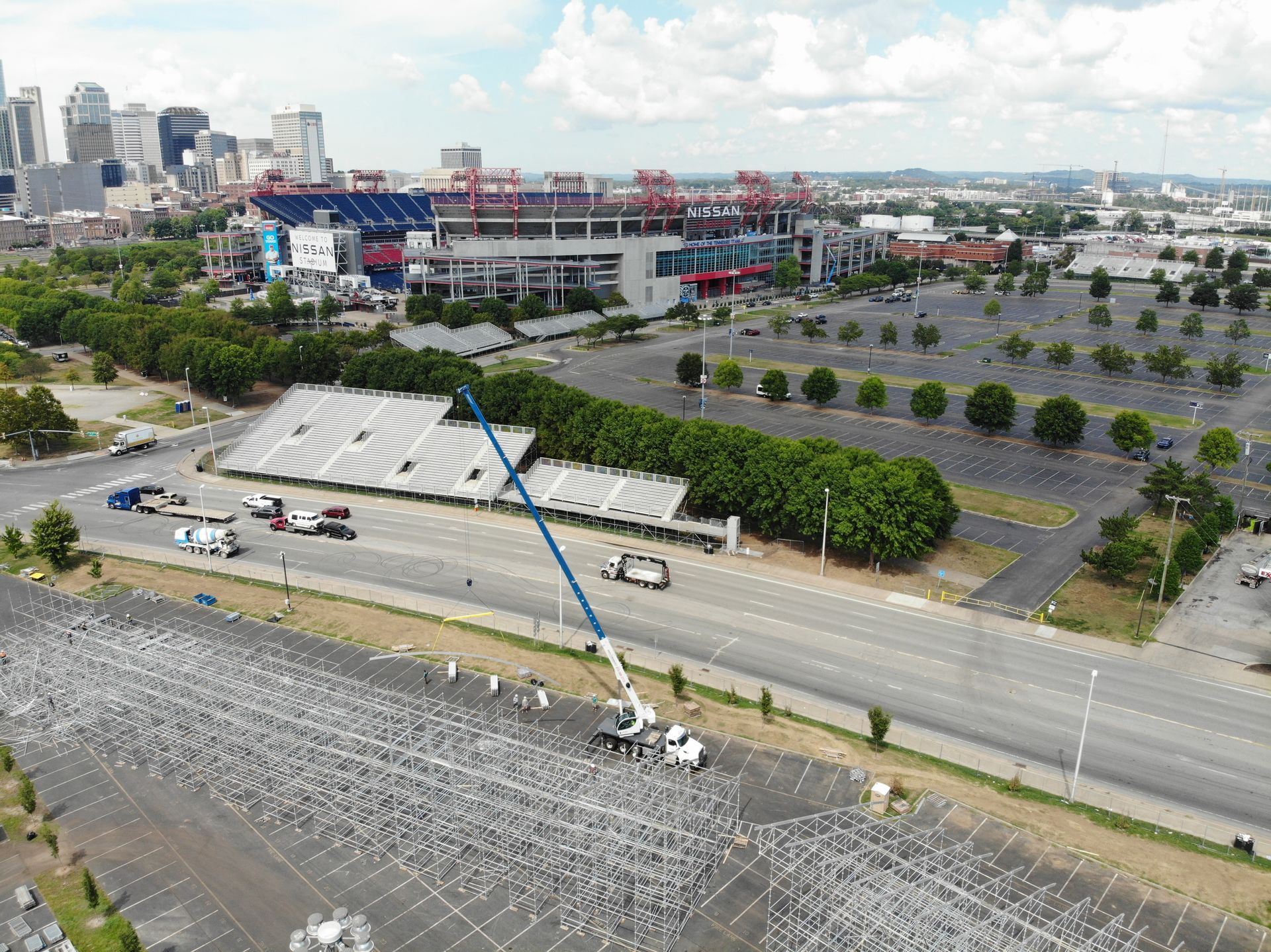 Construction of temporary structures in a parking lot near a stadium with a city skyline in the background.