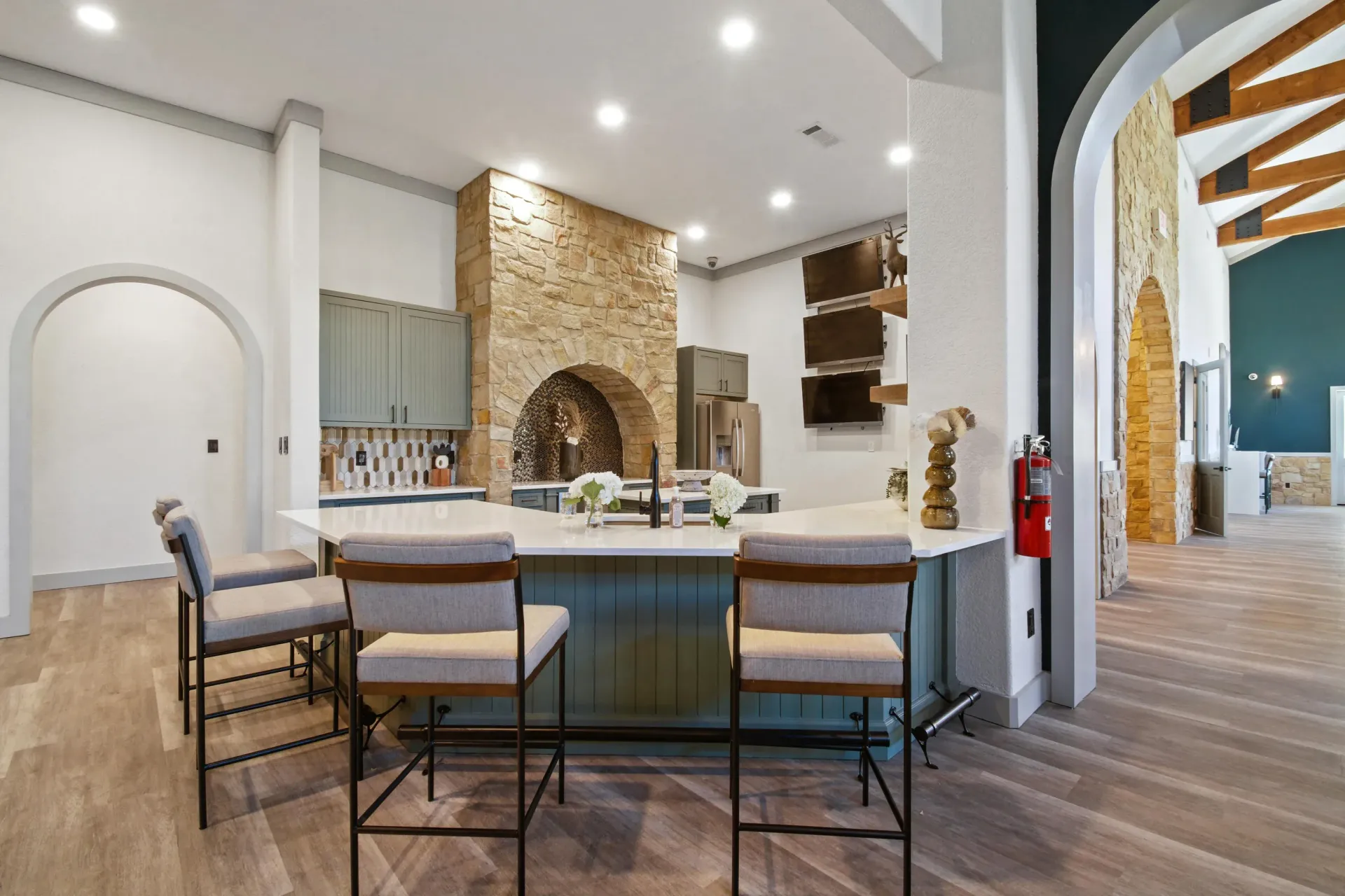 Dining room with long wooden table, chairs, and art, leading to a kitchen with a bar.