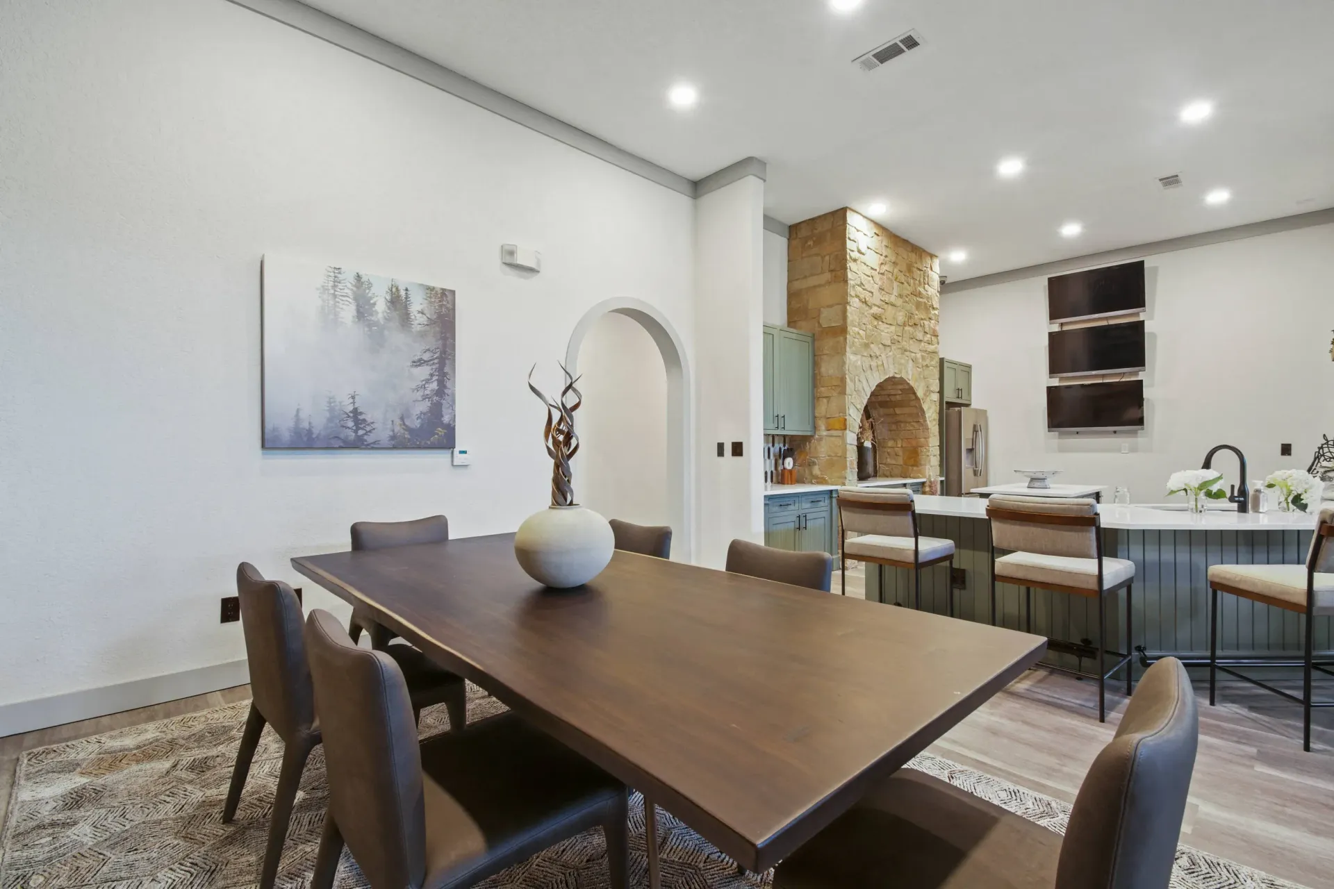 Spacious living area with stone fireplace, brown leather sofa, and large chandelier. Wooden floors and high ceilings.