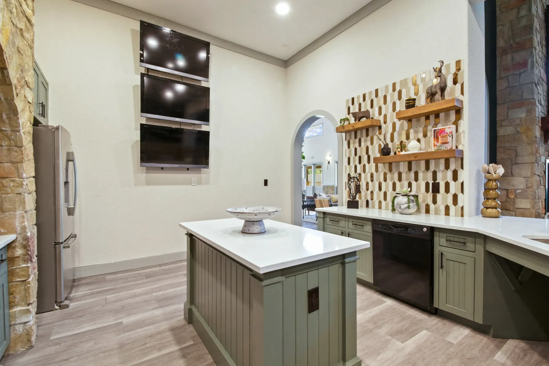 A room with a stone fireplace, pool table, arched doorways, and light wood flooring.