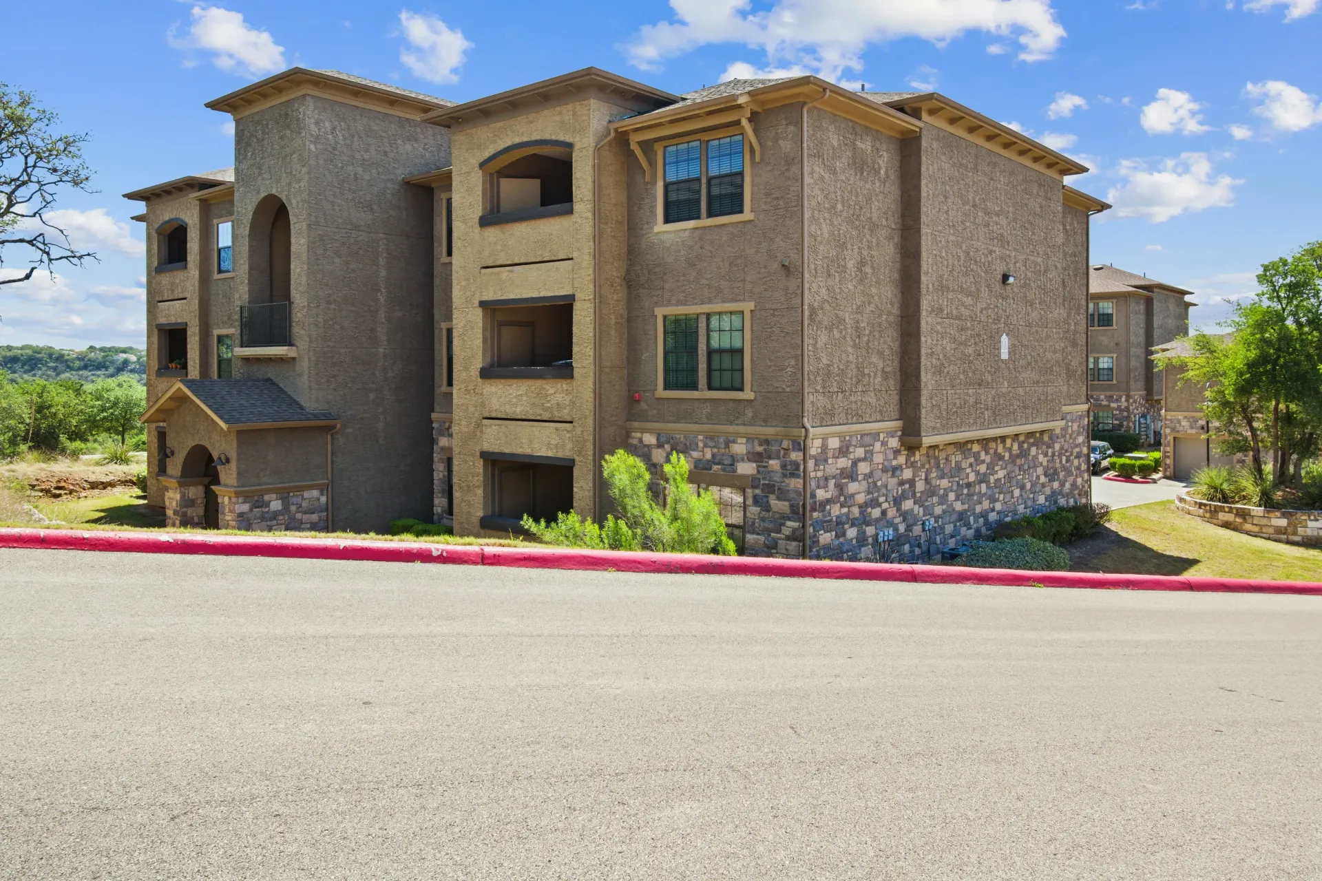 Multi-story apartment building with stone and stucco exterior, set on a hillside.