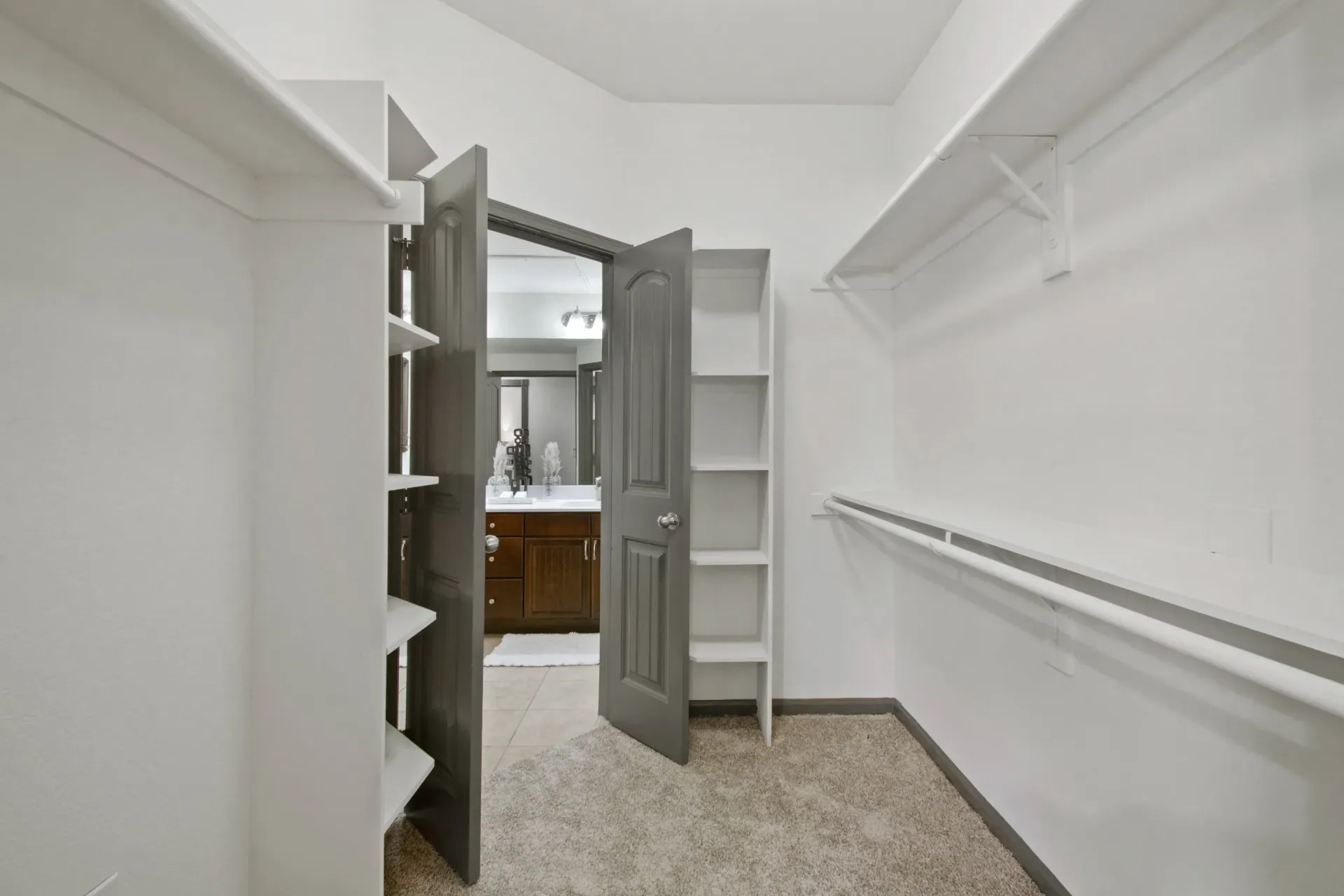 Walk-in closet with shelves and rod. Open door leads to a bathroom with a vanity.