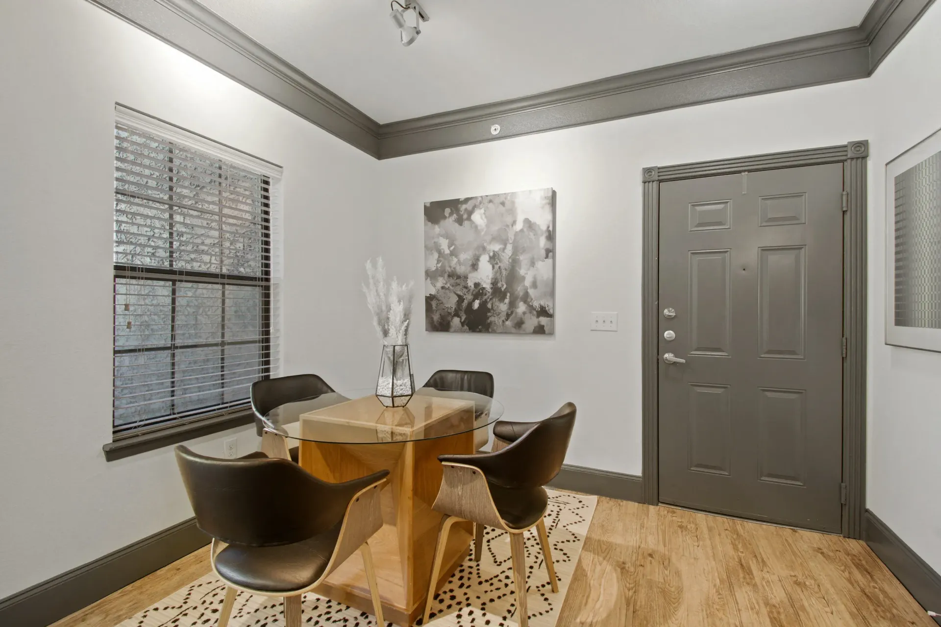 Lobby room with table and chairs.  Gray trim and door.  Window with blinds. Artwork on wall.