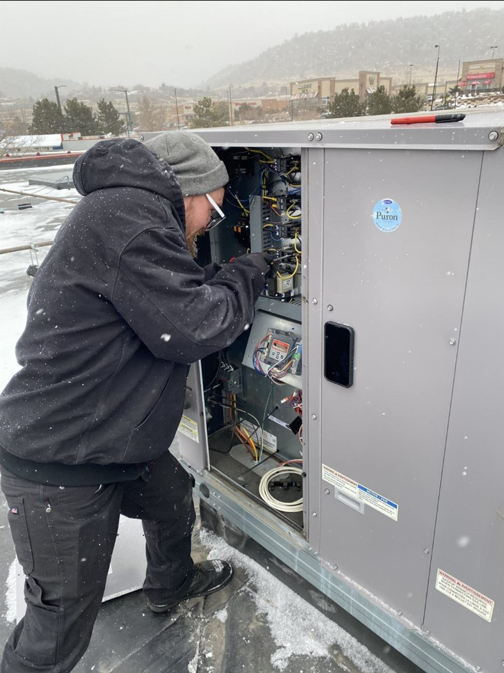 A man is working on a rooftop air conditioner.
