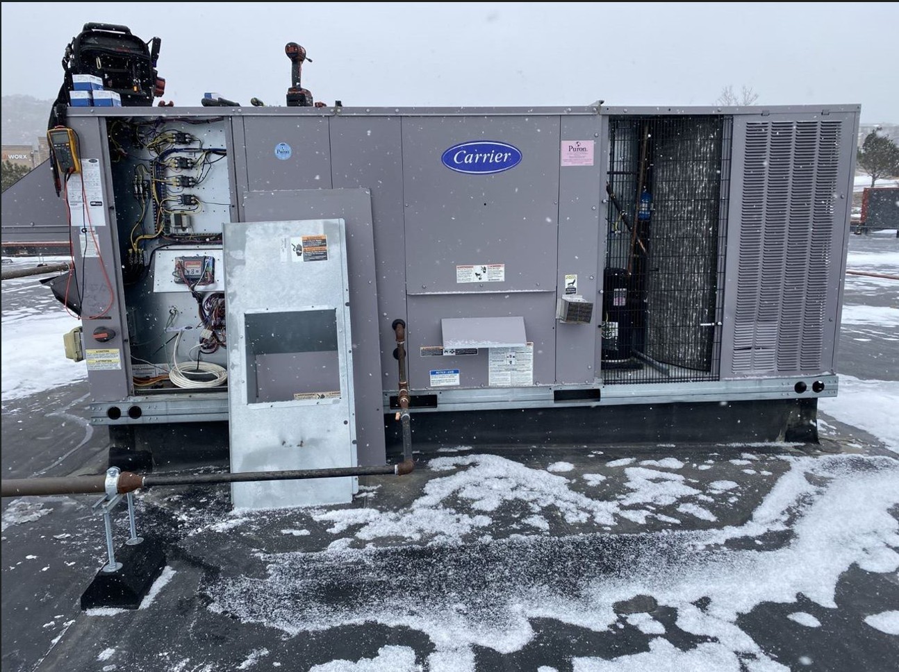 A carrier air conditioner is sitting on top of a snow covered roof.