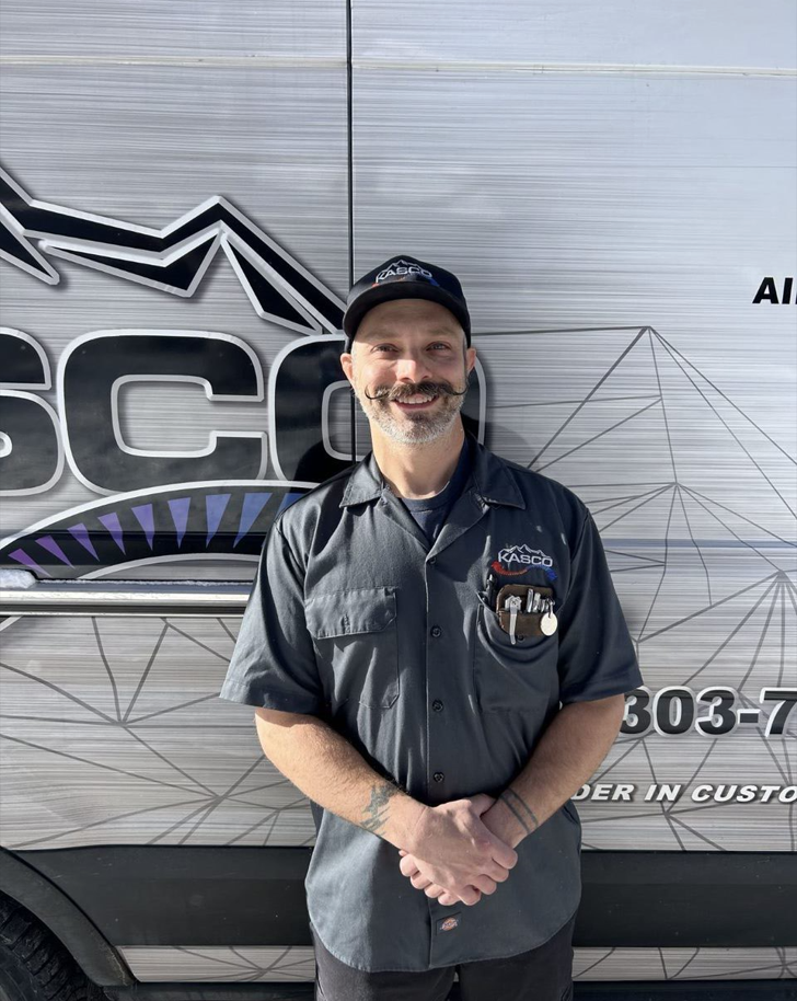 A man with a mustache is standing in front of a van.