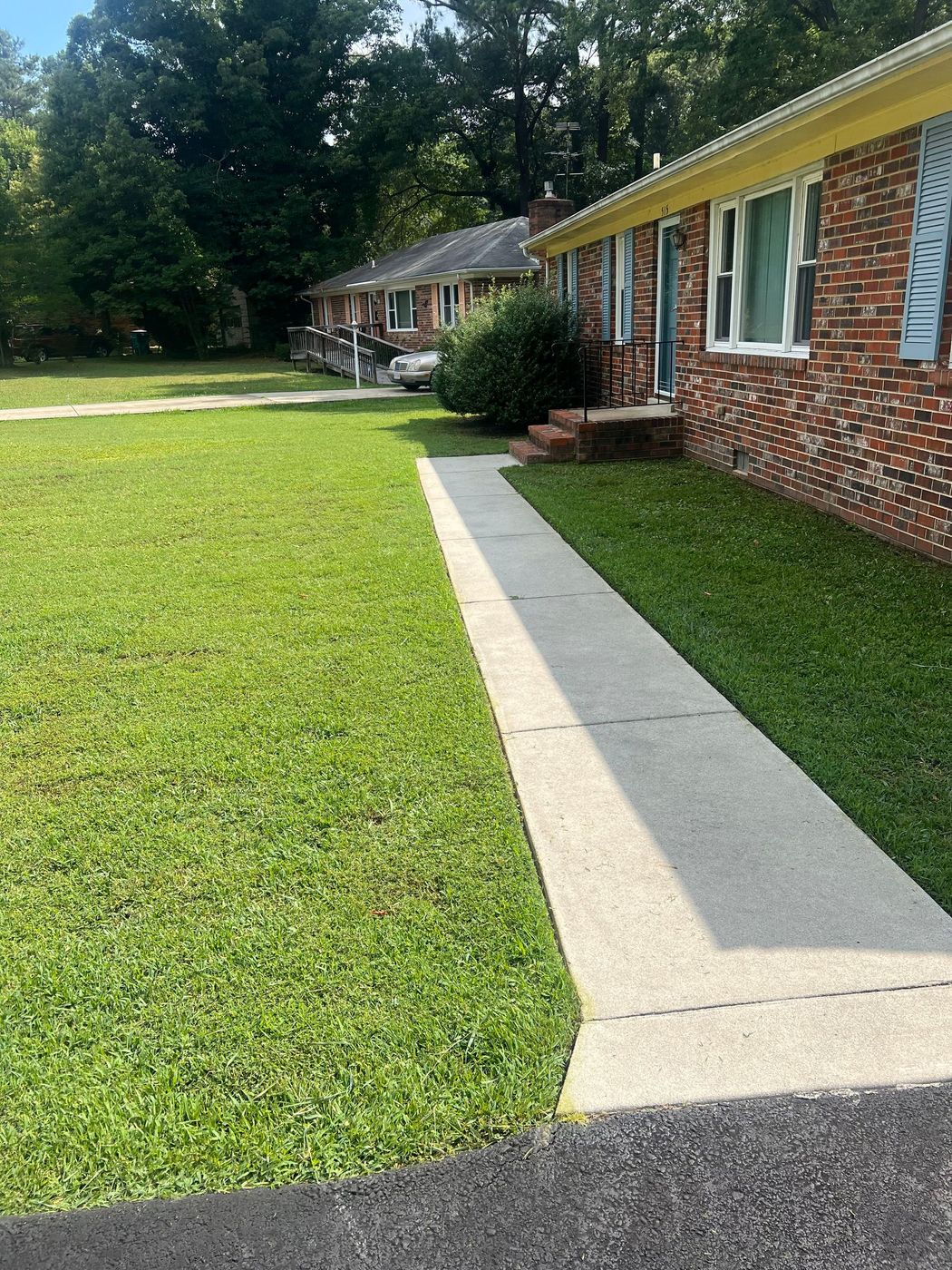 A brick house with a lush green lawn and a sidewalk in front of it.