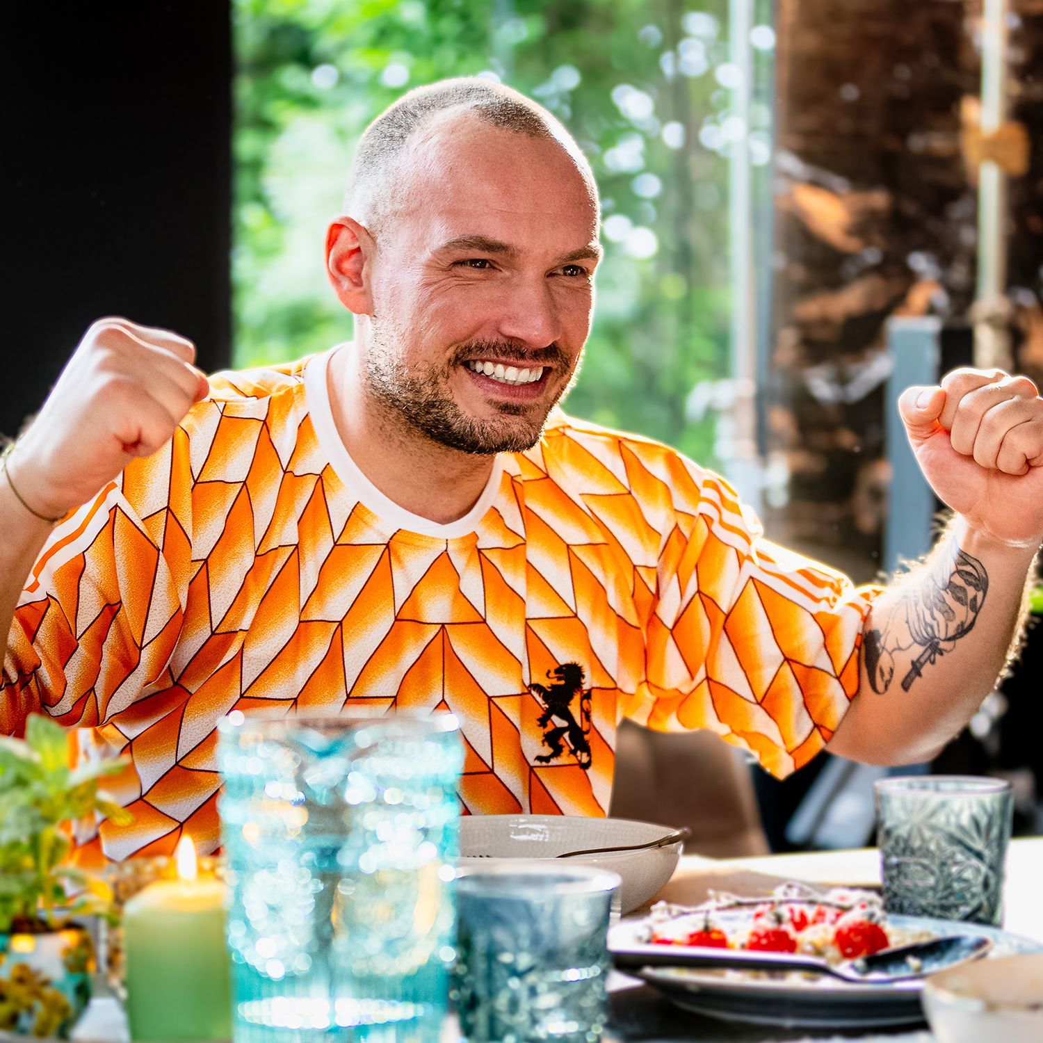 Een man met een oranje shirt zit aan een tafel.