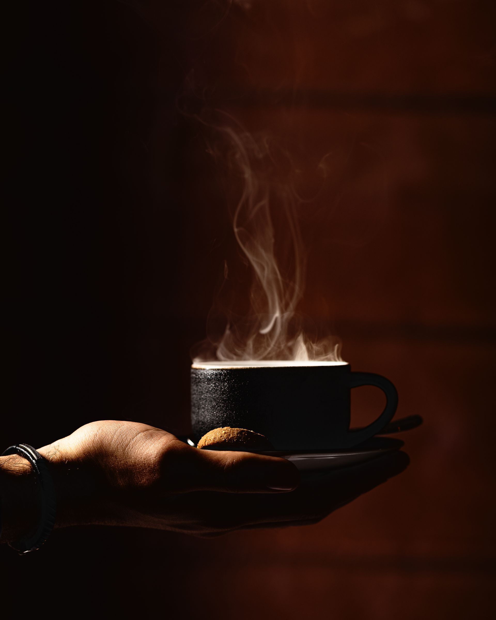 Hand die een dampende zwarte koffiemok vasthoudt tegen een donkere achtergrond.