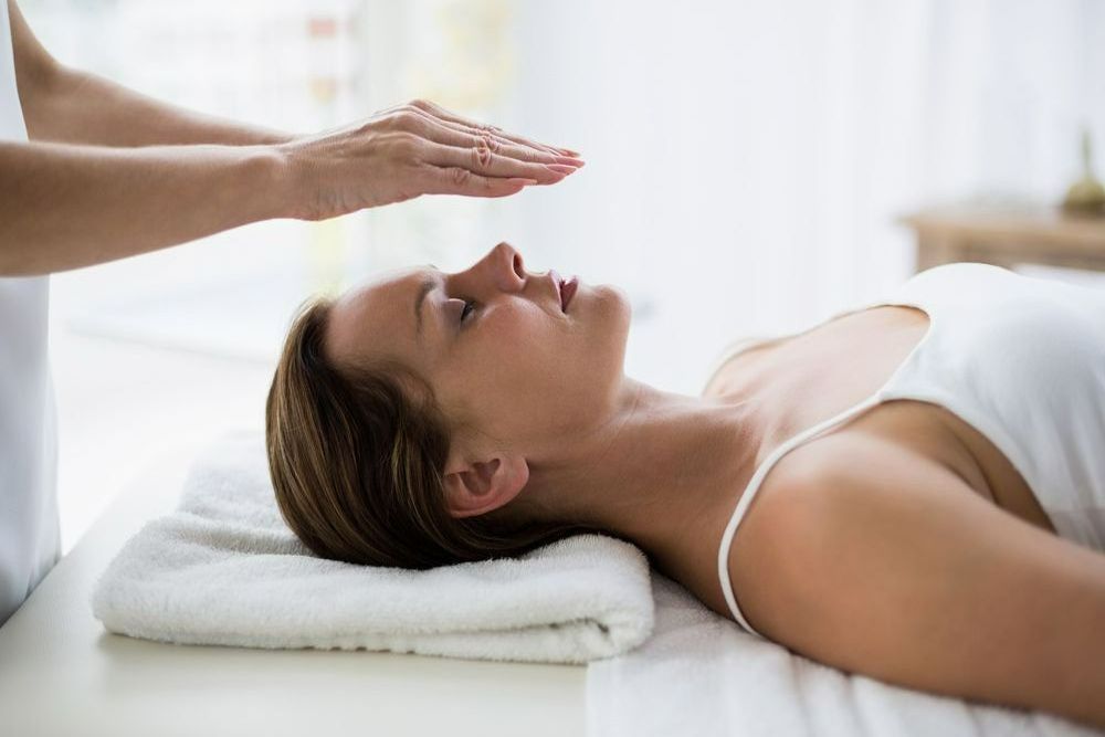 A Woman Is Laying On A Bed Getting A Reiki Session — Chez Belle Skin Care & Beauty Centre in Pimlico, QLD
