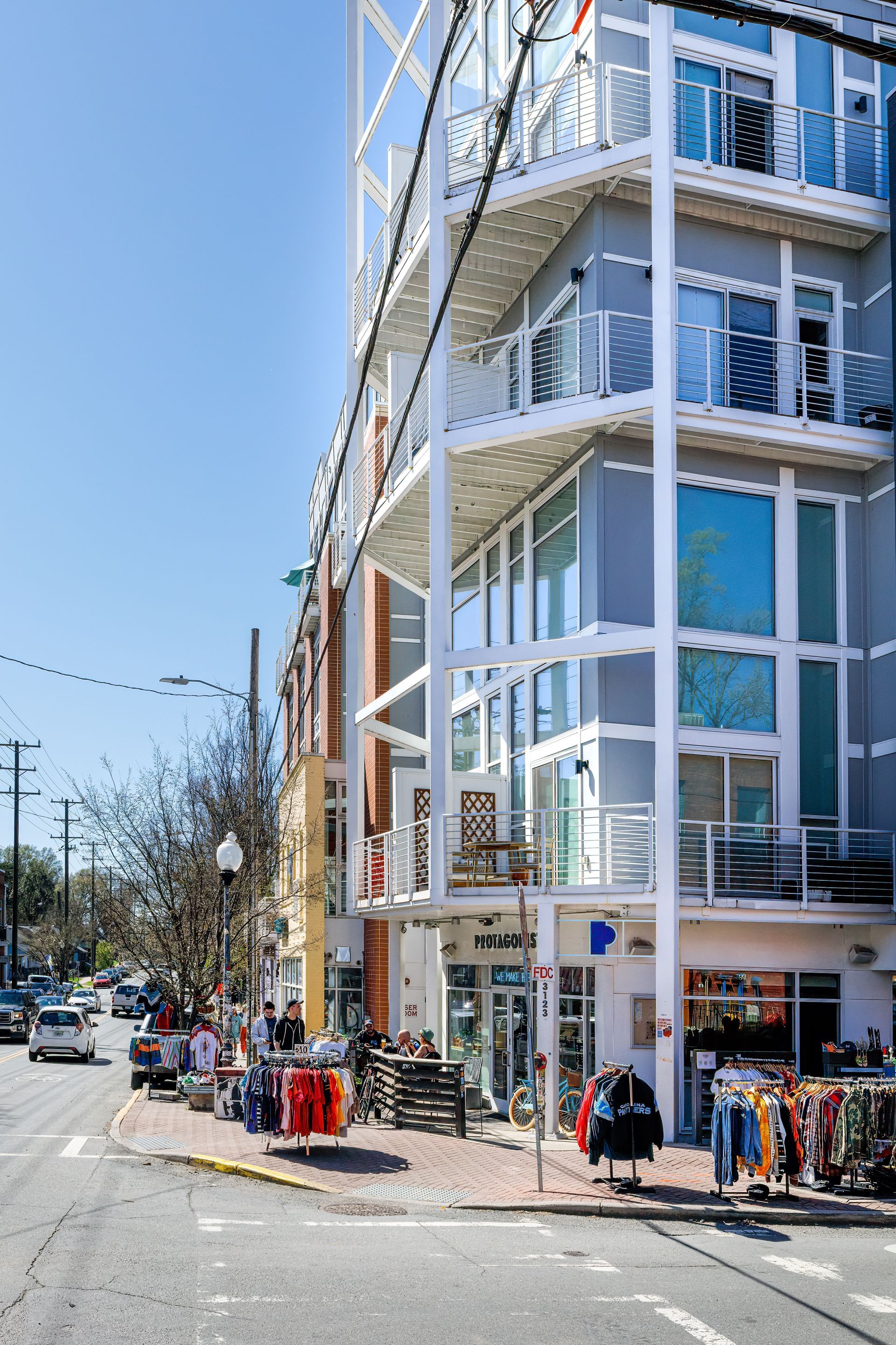 Street view of a colorful multi-story building with balconies, people, and shops on a sunny day in NoDa, Charlotte