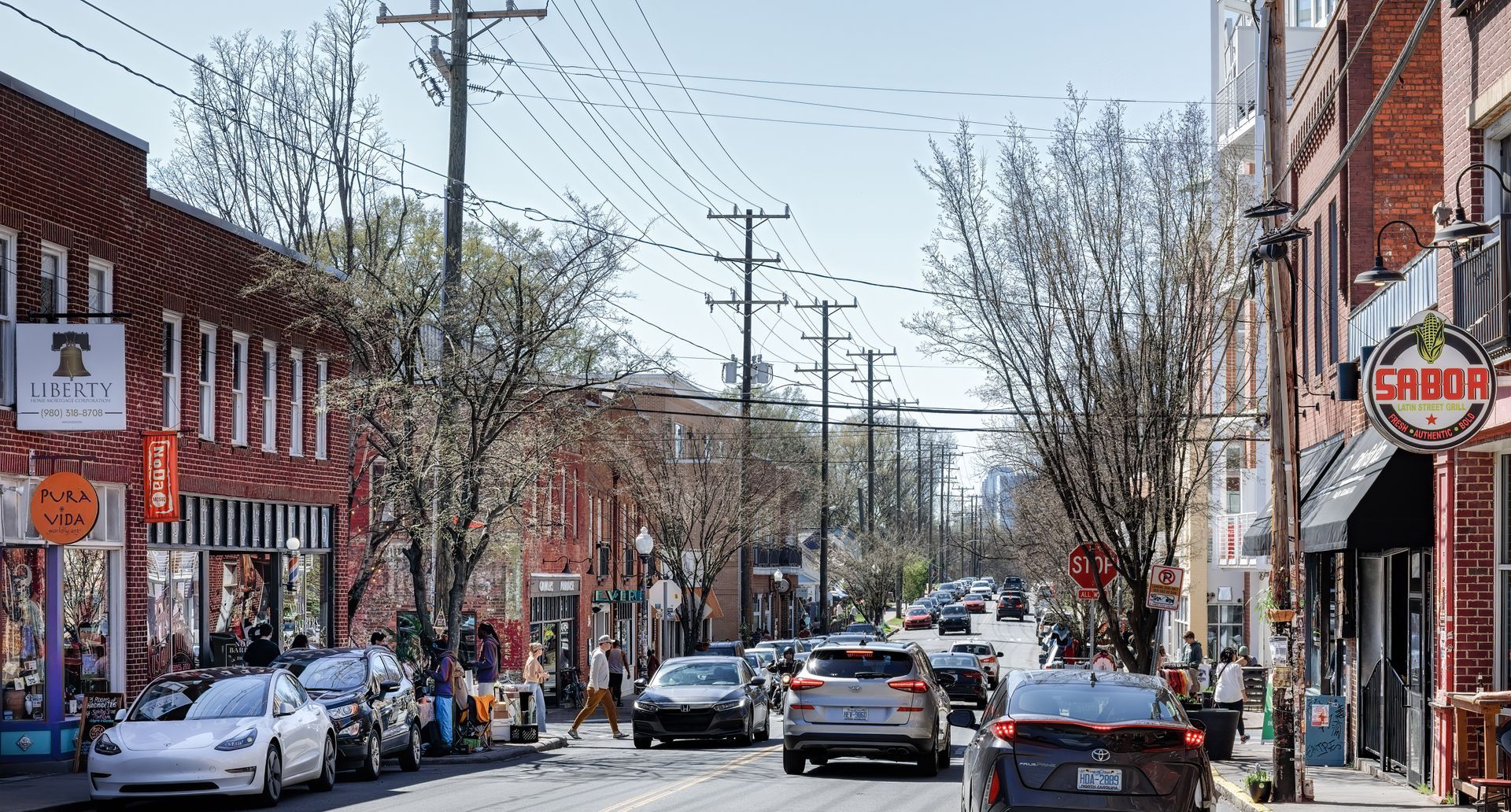 Street with cars, shops, and trees; sunny day in NoDa Charlotte