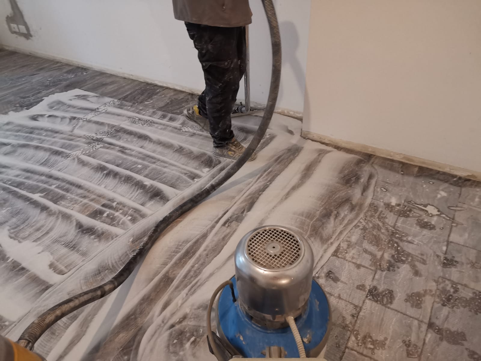 Persona che carteggia un pavimento in legno con polvere bianca che ricopre le assi.