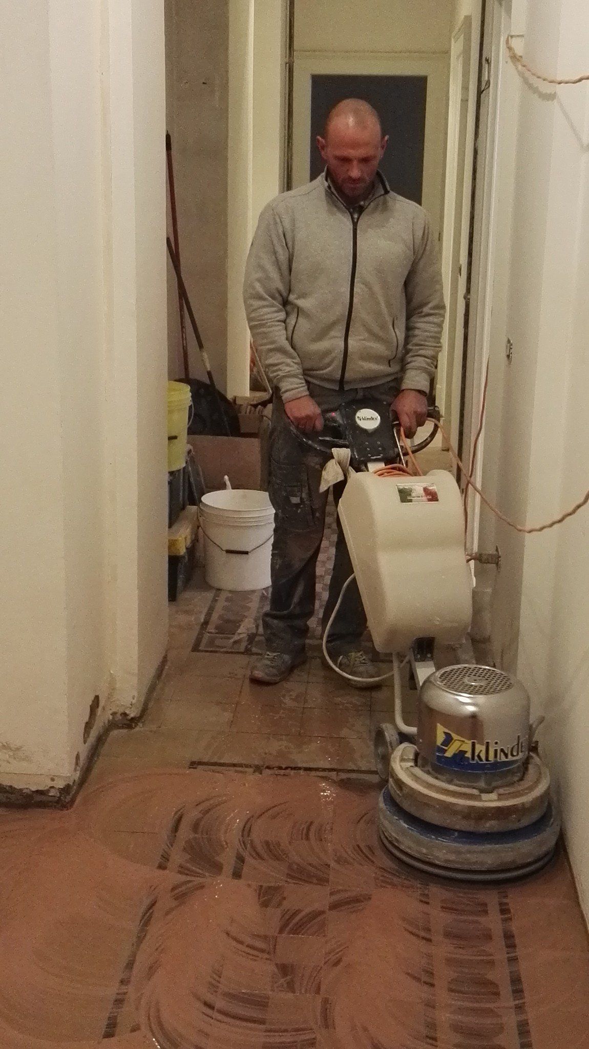 Uomo che leviga il pavimento di un corridoio con una grande levigatrice industriale.